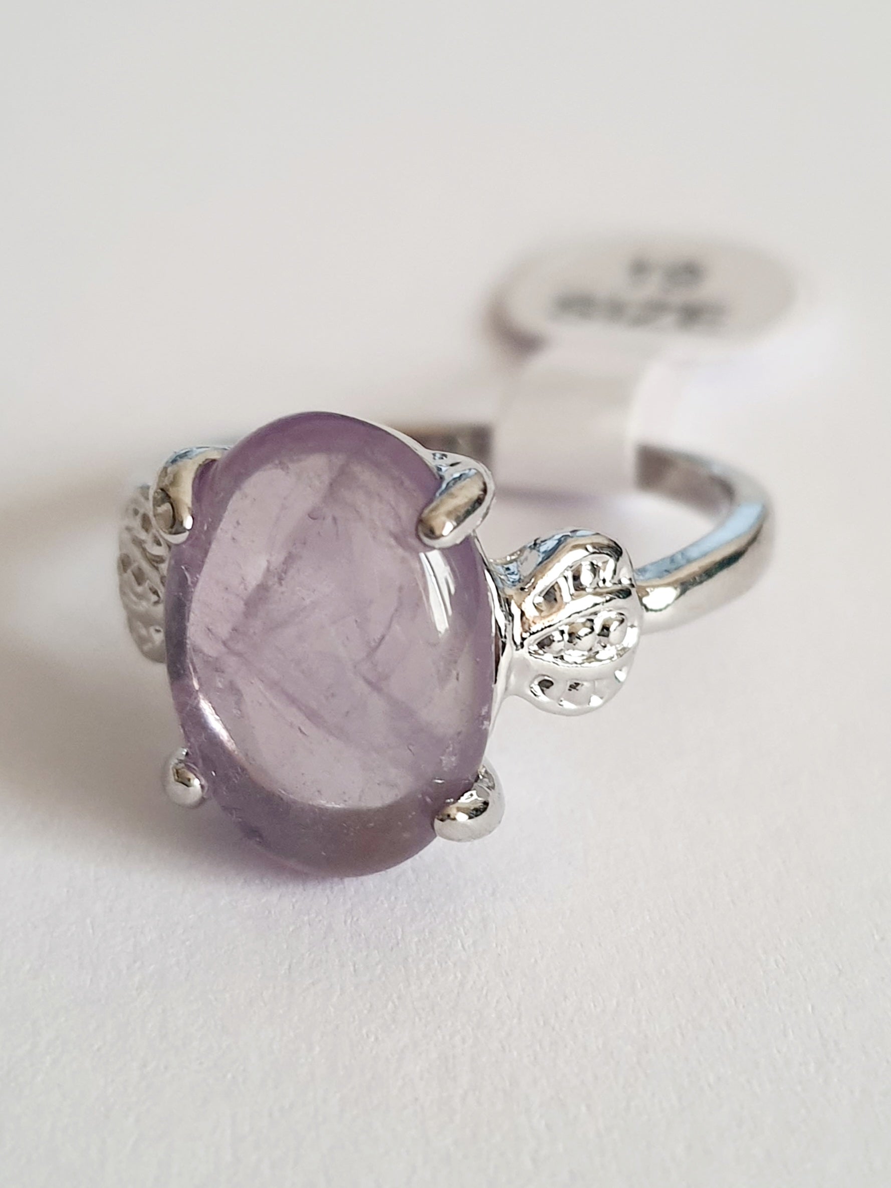 Pierścionek ze stali chirurgicznej w srebrnym kolorze z jasnofioletowym, owalnym kamieniem w stylu ametystu. Boczne elementy w kształcie liści. Styl romantyczny i subtelny. Rozmiar 19 mm. Rouge Bizu.