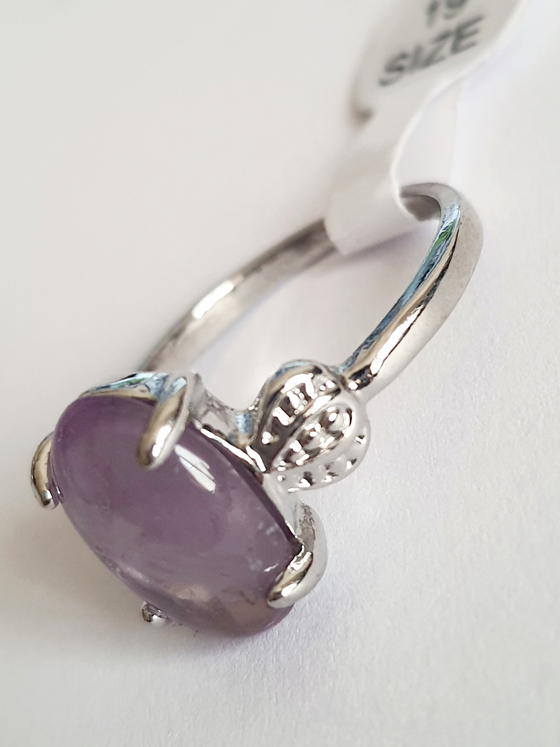 Pierścionek ze stali chirurgicznej w srebrnym kolorze z jasnofioletowym, owalnym kamieniem w stylu ametystu. Boczne elementy w kształcie liści. Styl romantyczny i subtelny. Rozmiar 19 mm. Rouge Bizu.