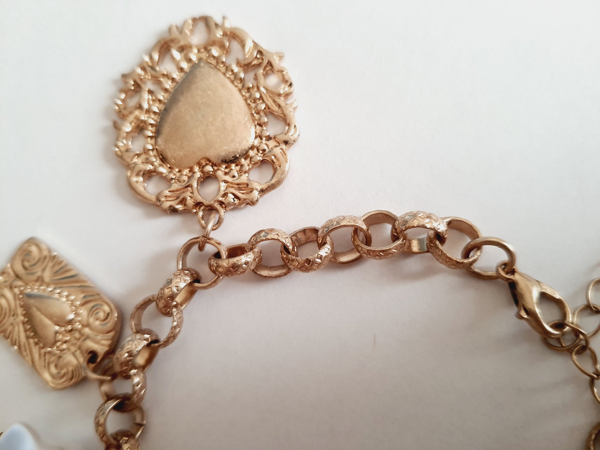 Złota bransoletka w stylu vintage z charmsami: serca, symbole sakralne, perłowe zawieszki. Stal chirurgiczna, długość regulowana 20–28 cm. Klasyka, romantyzm i mistyczna elegancja. Rouge Bizu.