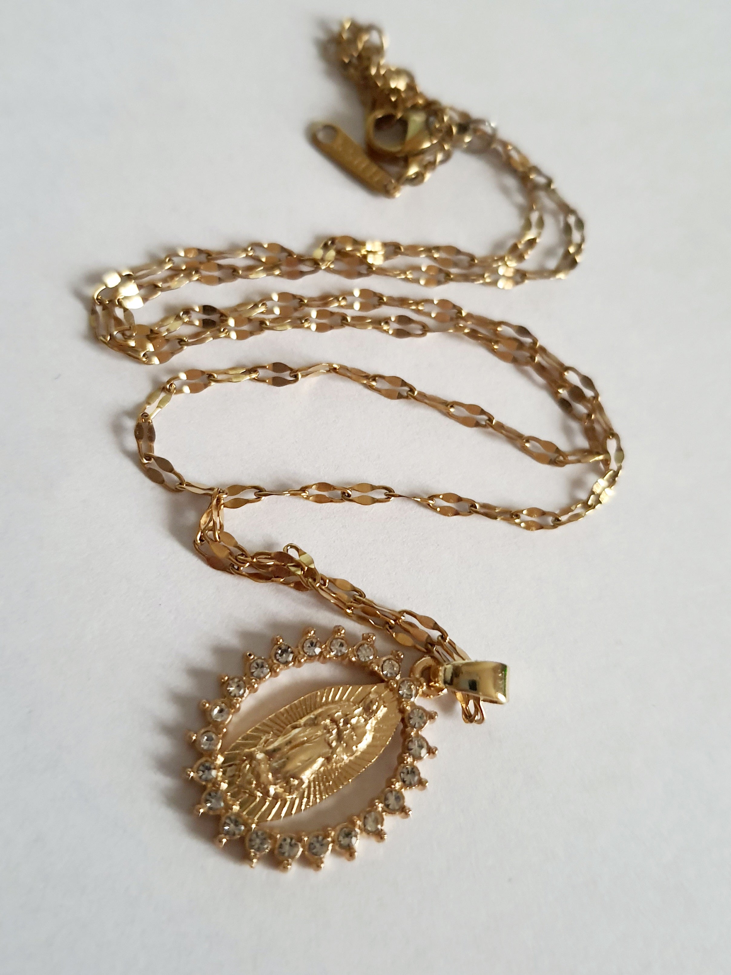 Złoty łańcuszek o długości 40–46 cm z wisiorkiem Matki Boskiej otoczonym cyrkoniami. Styl sakralny, elegancki. Stal nierdzewna, Rouge Bizu.