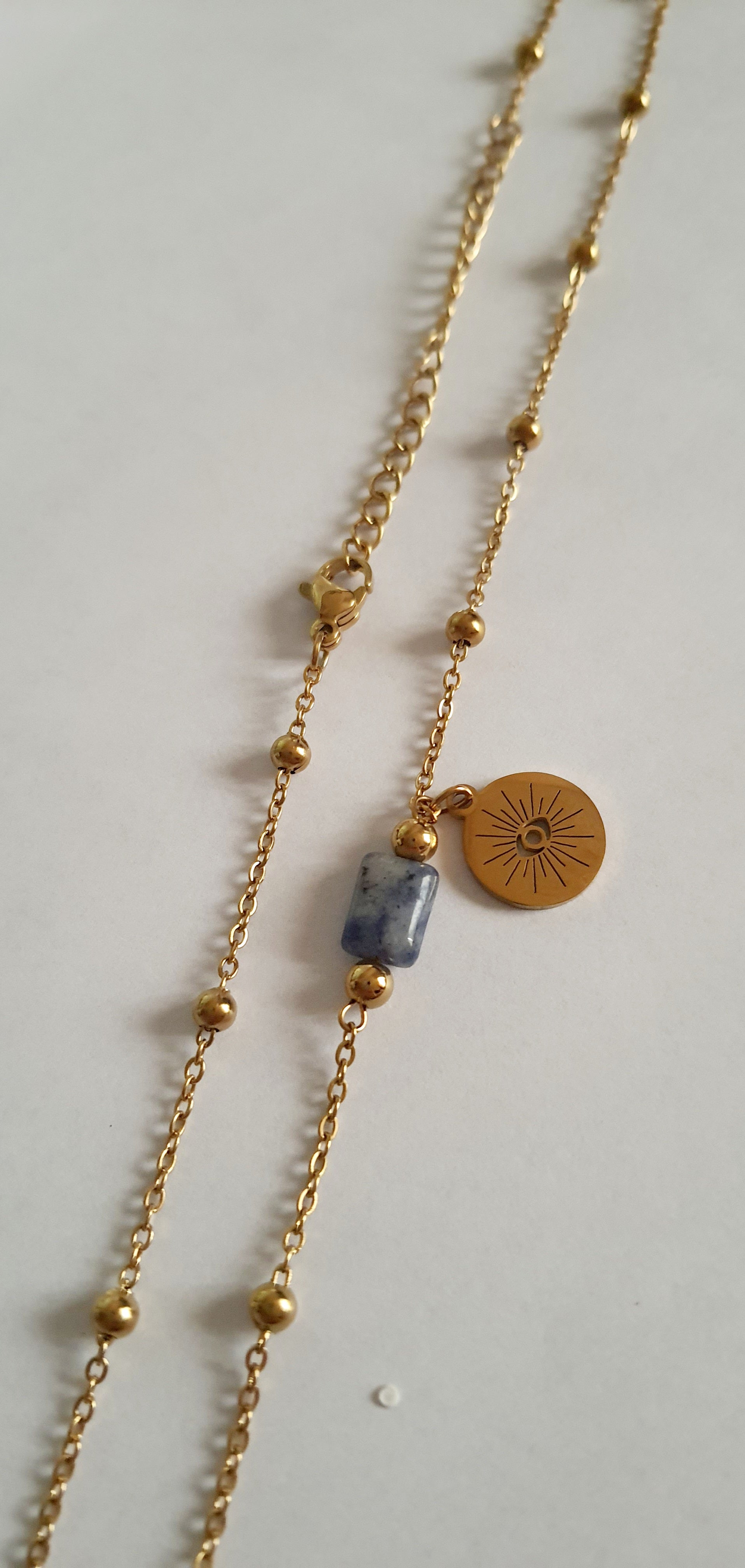 Złoty łańcuszek ze stali nierdzewnej o długości 40–45 cm z granatowym kamieniem i okrągłym talizmanem w kształcie słońca. Styl boho, minimalistyczny, duchowy. Rouge Bizu.