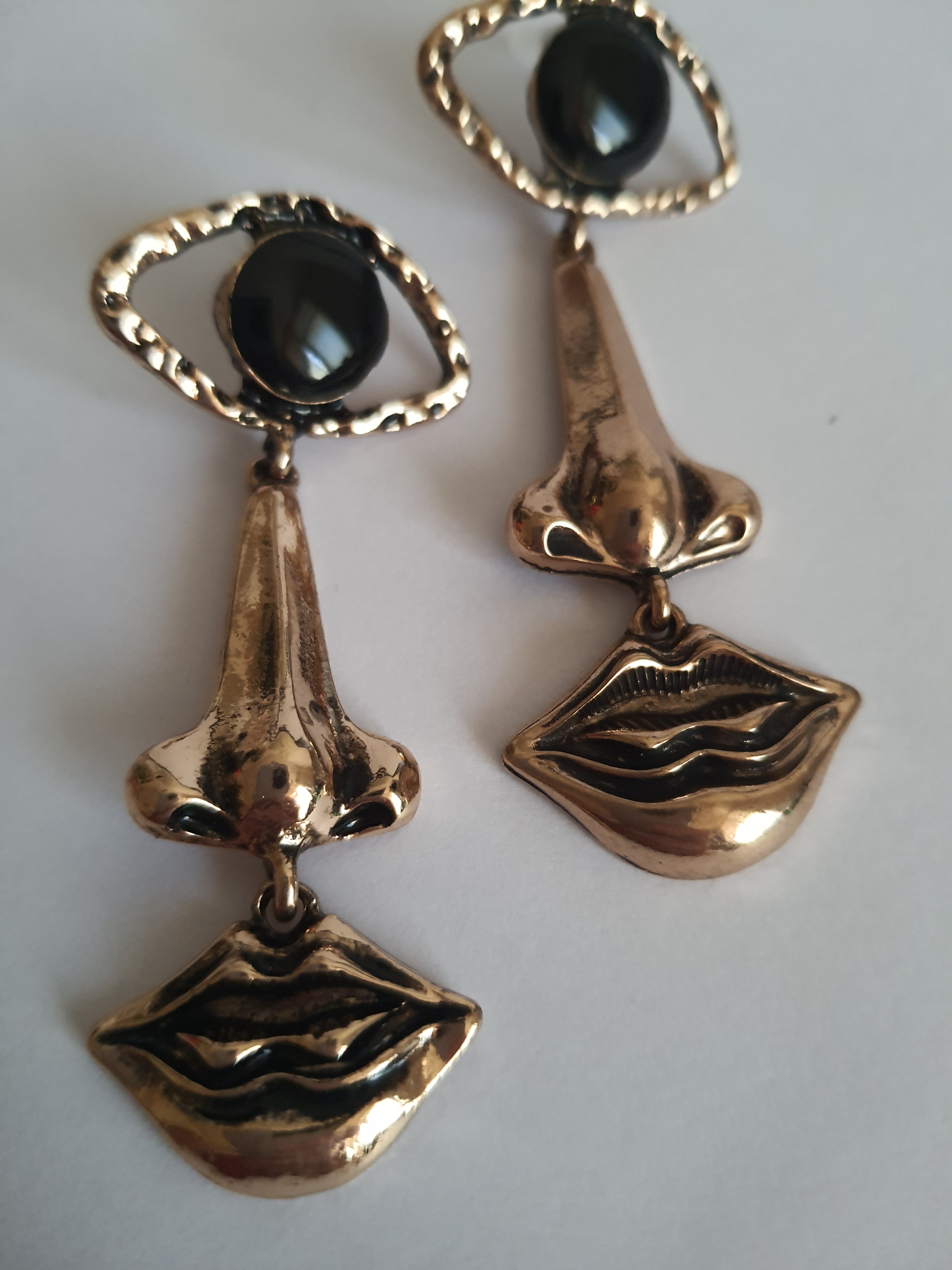 Wiszące kolczyki 7 cm ze stali nierdzewnej w kolorze złotym w kształcie oka, nosa i ust, z czarnym kamieniem w centrum oka. Rouge Bizu, stal nierdzewna, stal chirurgiczna.