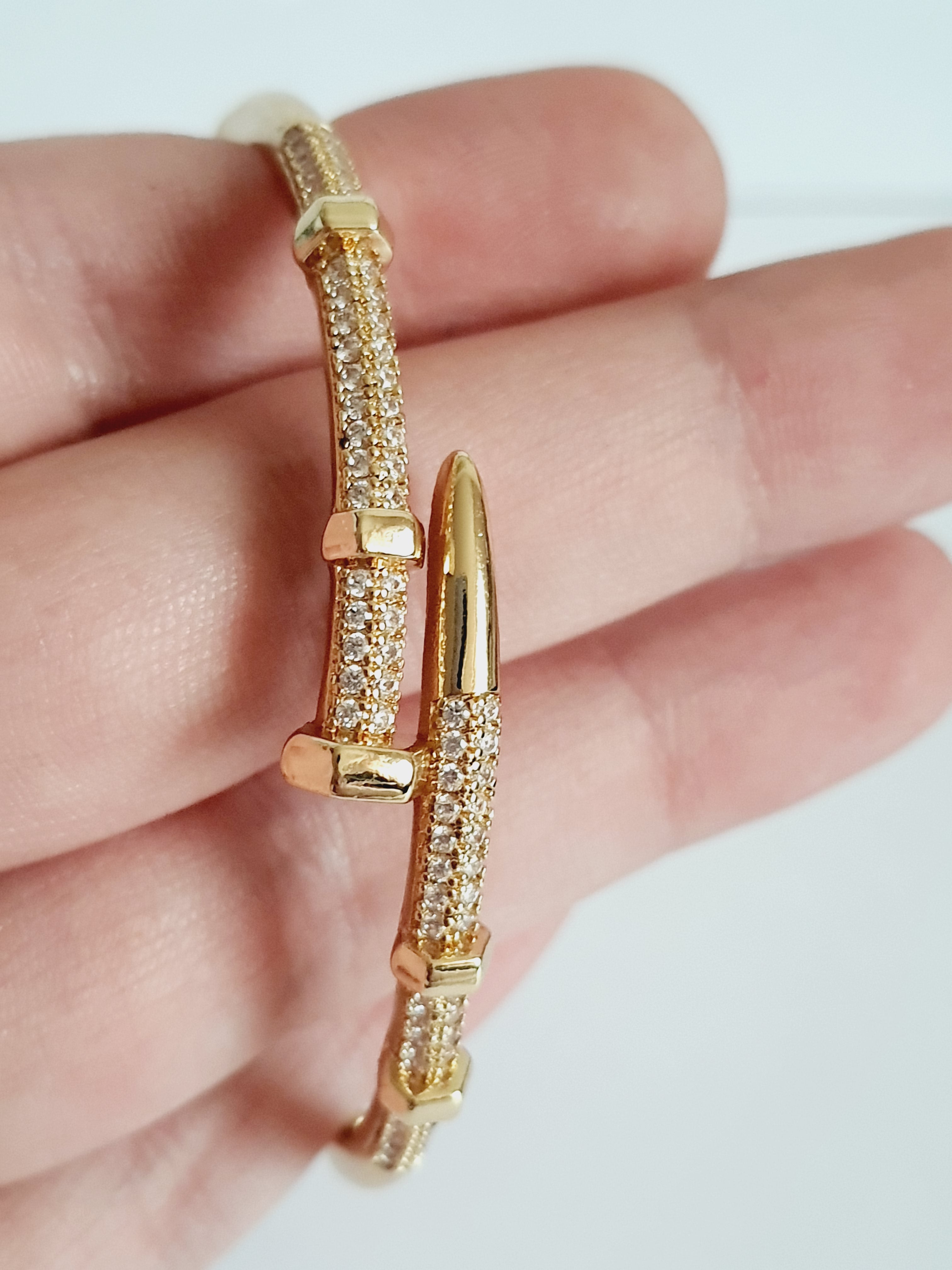 Złota bransoletka sztywna o średnicy 6 cm, zdobiona białymi cyrkoniami, nowoczesny elegancki design, stal nierdzewna. Rouge Bizu.