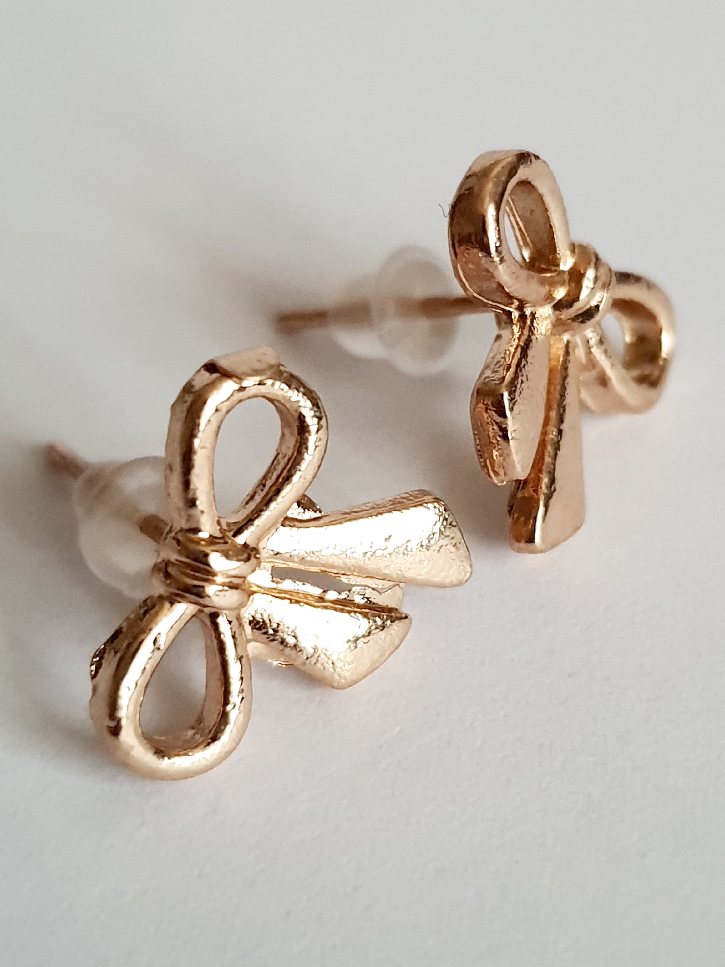 Złote kolczyki kokardki wkrętki, stal nierdzewna, długość 1,5 cm, subtelny romantyczny styl. Rouge Bizu.