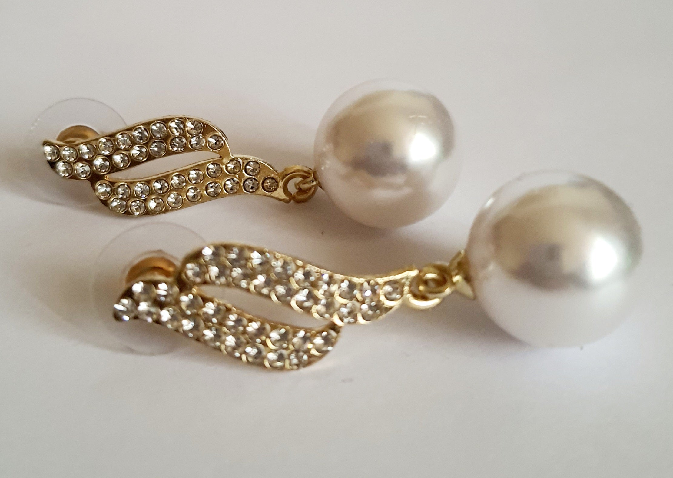 Kolczyki złote ze stali nierdzewnej o długości 4 cm, z dużą białą perłą i złotą falą wysadzaną cyrkoniami, elegancja i blask, Rouge Bizu.