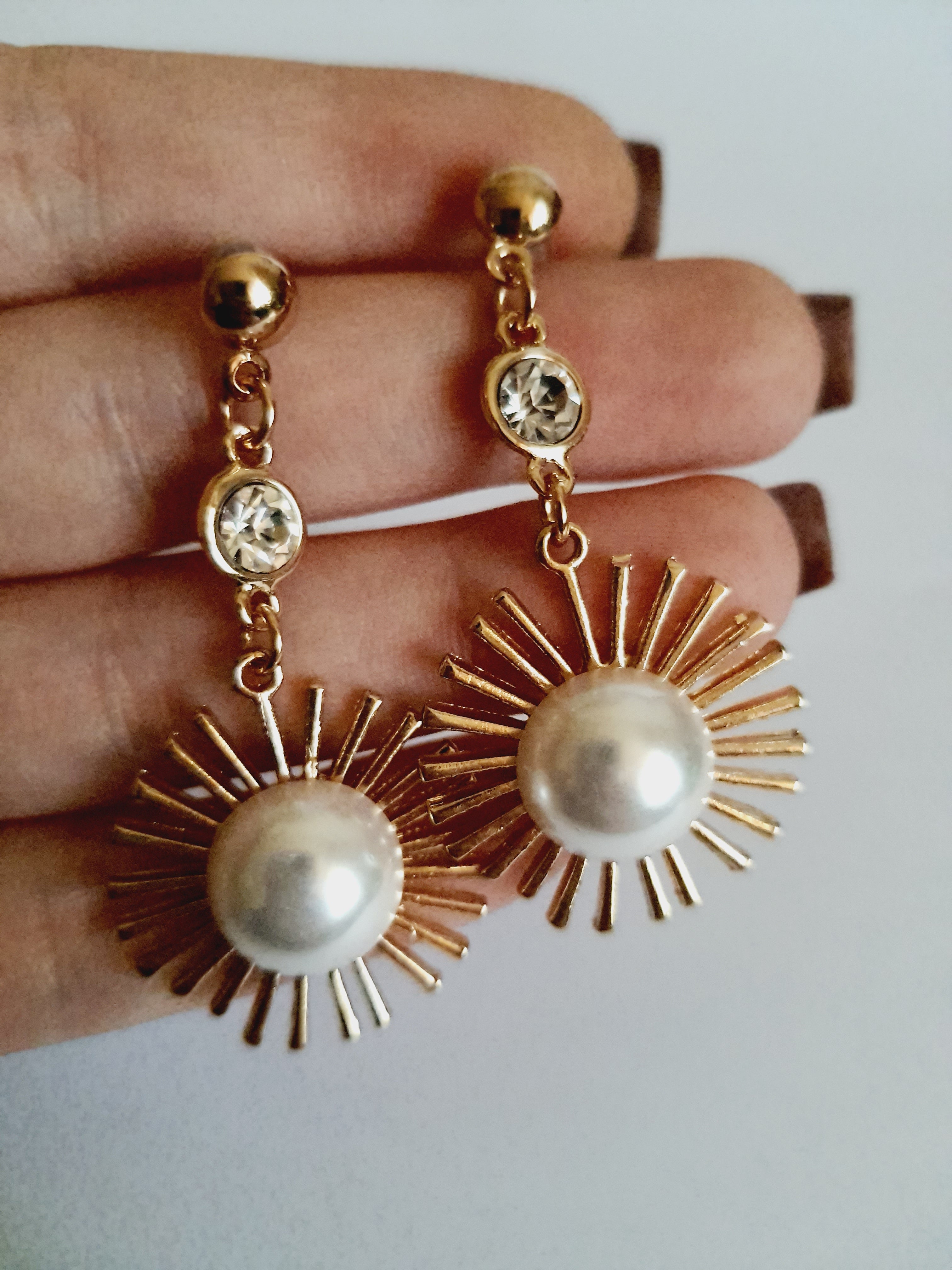 Złote kolczyki wiszące 5 cm, z białą perłą w centrum i promienistą oprawą, u góry kryształek – elegancki design inspirowany słońcem, Rouge Bizu.