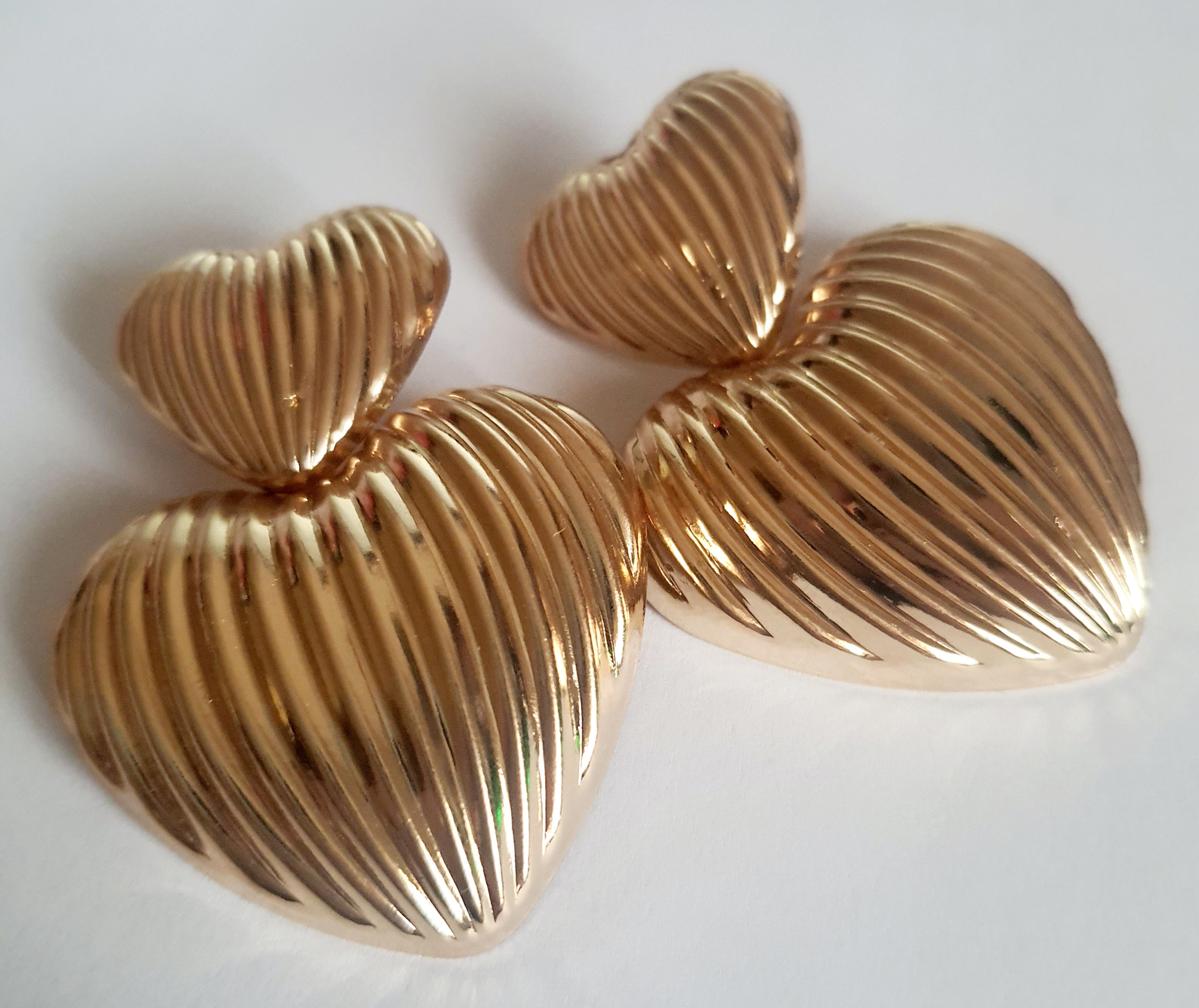 Złote kolczyki w kształcie serc, duże i eleganckie, ze żłobieniami nadającymi im wyjątkowego blasku. Wykonane ze stali nierdzewnej. Rouge Bizu.