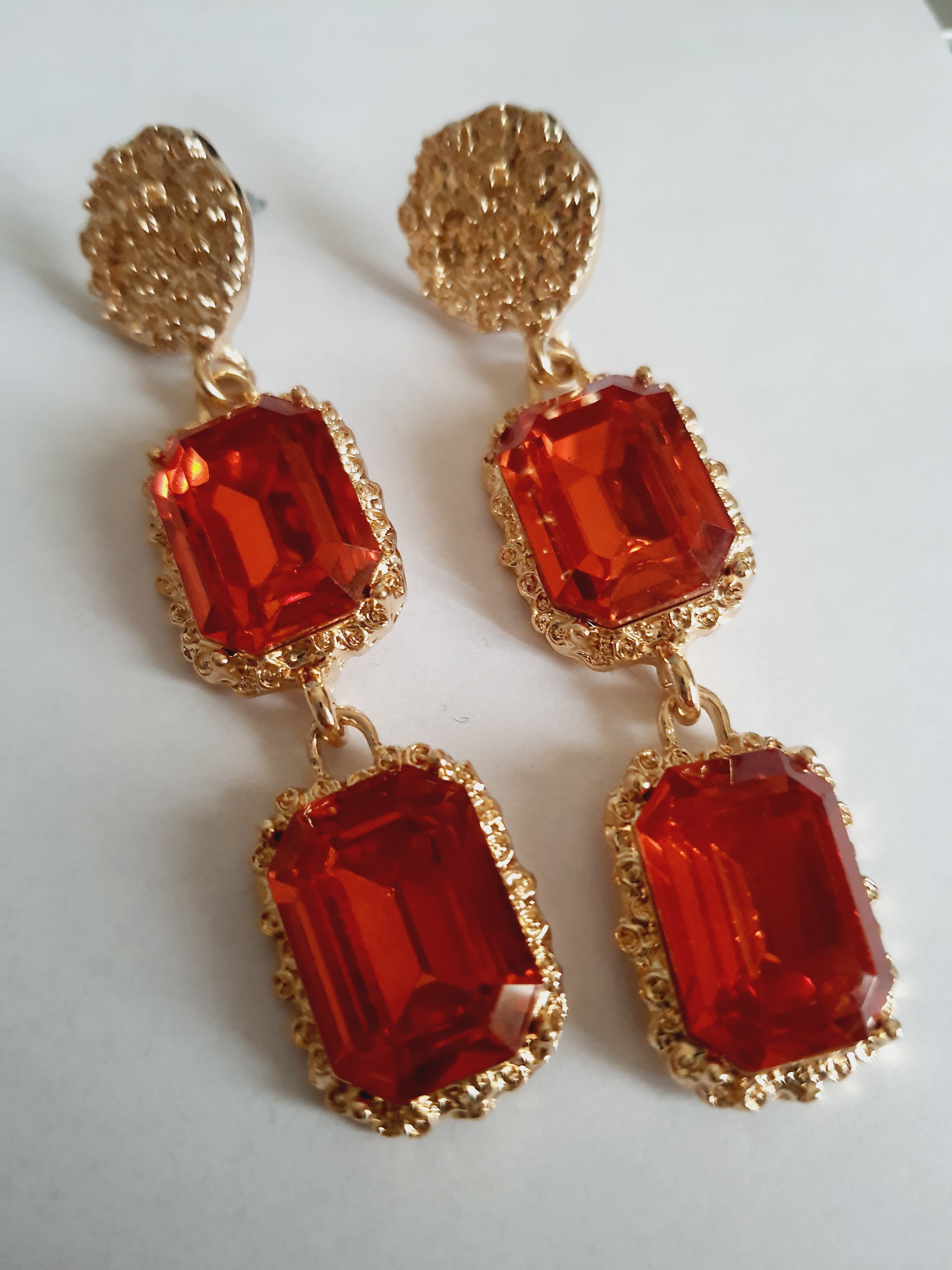 Długie kolczyki ze stali nierdzewnej w stylu glamour, ozdobione dużymi czerwonymi kamieniami w złotej oprawie. Elegancja, luksus i ognisty blask. Długość 7 cm. Rouge Bizu.