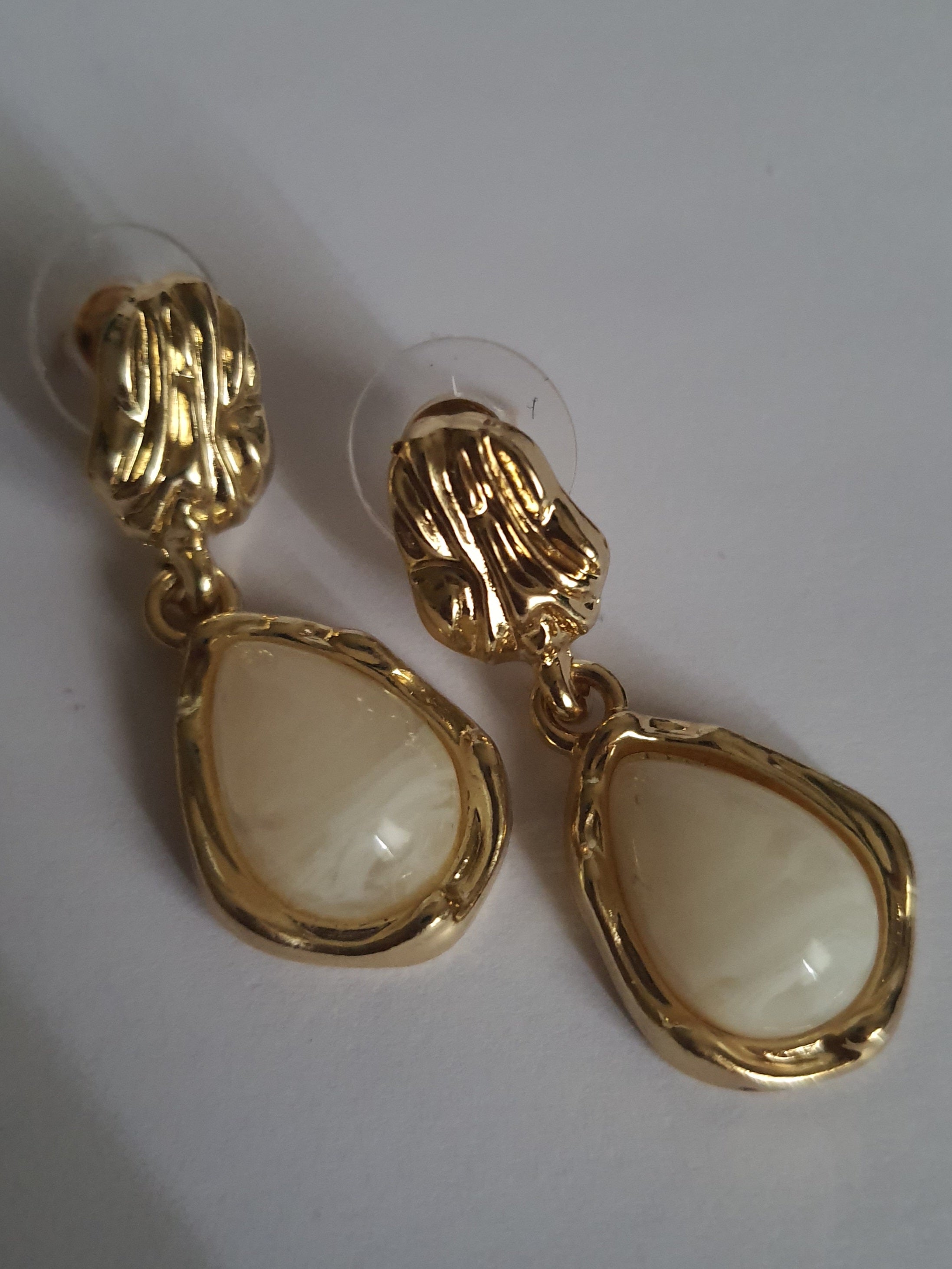 „Złote kolczyki ze stali nierdzewnej o długości 3 cm, zdobione perłowym kaboszonem w kształcie kropli, eleganckie i klasyczne – Rouge Bizu.”