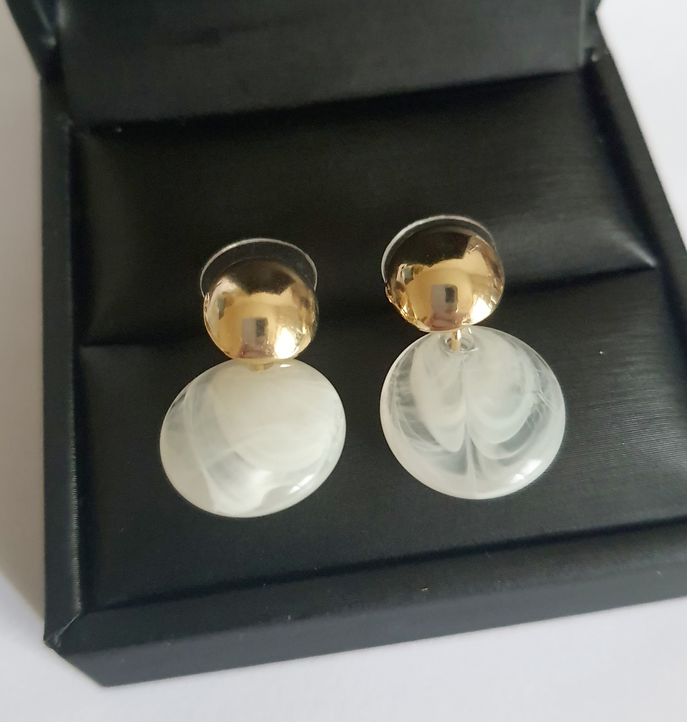 „Złote kolczyki ze stali nierdzewnej o długości 2,5 cm, z perłowym dyskiem zawieszonym na złotym sztyfcie, minimalistyczne i eleganckie – Rouge Bizu.”