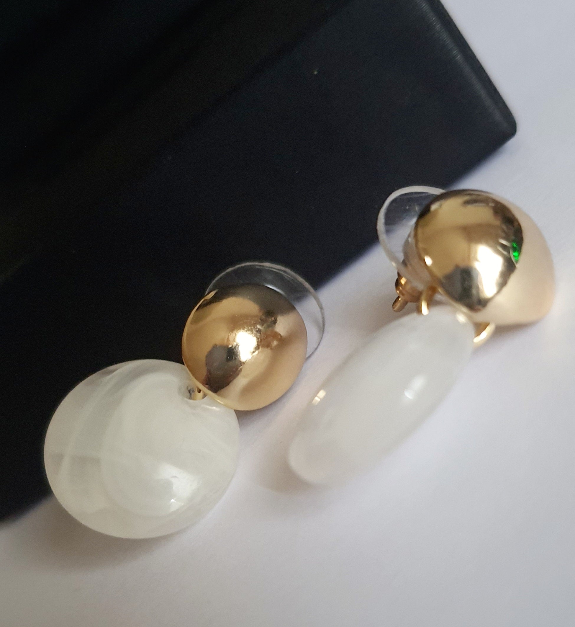 „Złote kolczyki ze stali nierdzewnej o długości 2,5 cm, z perłowym dyskiem zawieszonym na złotym sztyfcie, minimalistyczne i eleganckie – Rouge Bizu.”