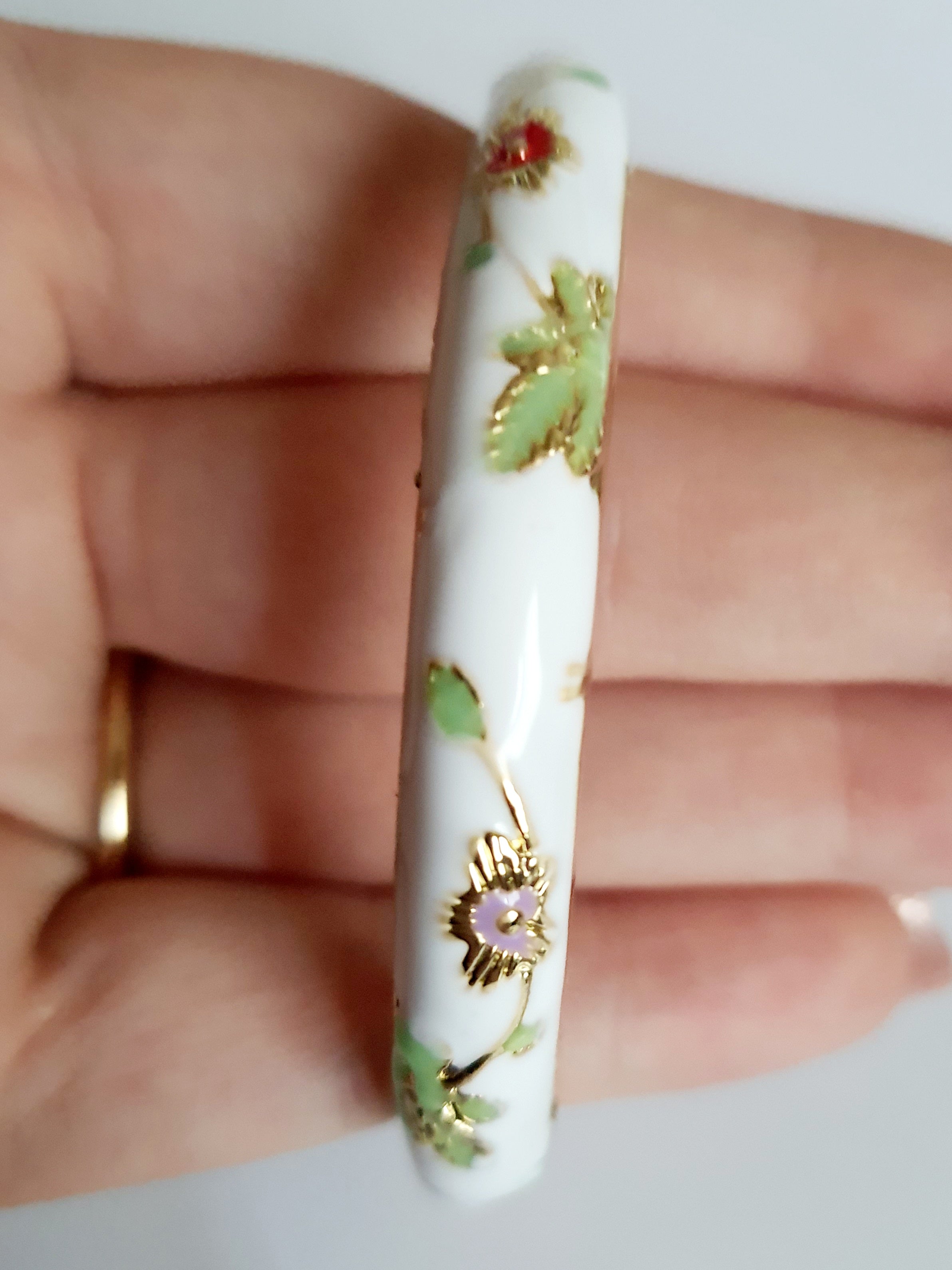 Bransoletka ze stali nierdzewnej, emaliowana na biało, zdobiona złotymi detalami i motywem kwiatowym w kolorach zieleni, czerwieni i różu, średnica 6 cm, Rouge Bizu.