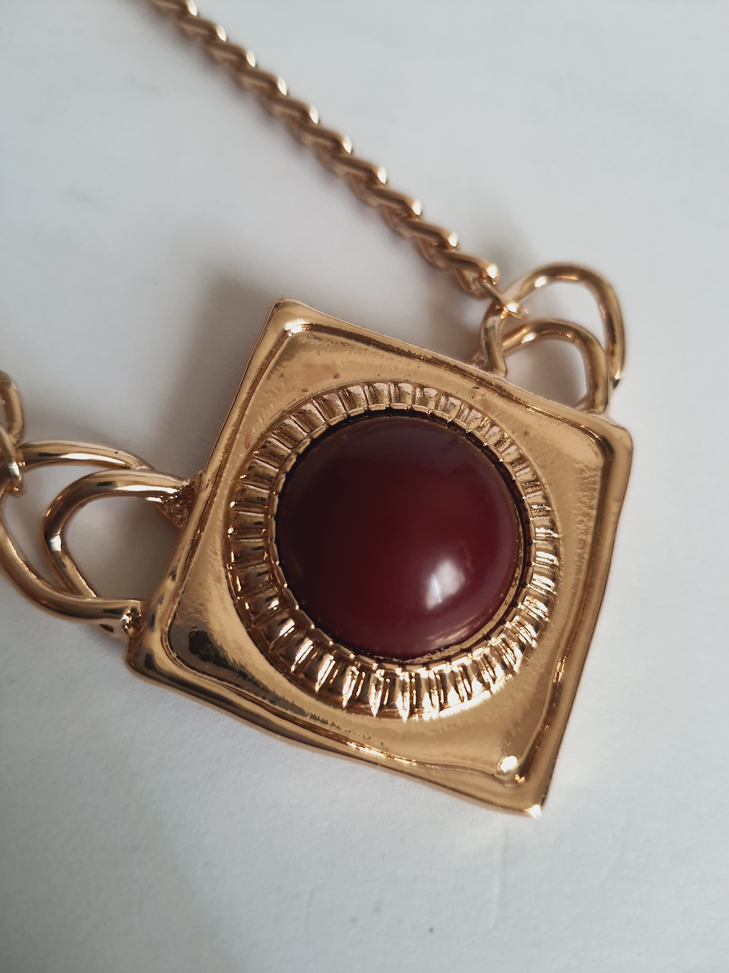 Naszyjnik ze stali nierdzewnej w kolorze złota, z geometryczną zawieszką w kształcie rombu i czerwonym kamieniem pośrodku. Styl elegancki, kobiecy, długość regulowana 44,5–54,5 cm. Rouge Bizu.