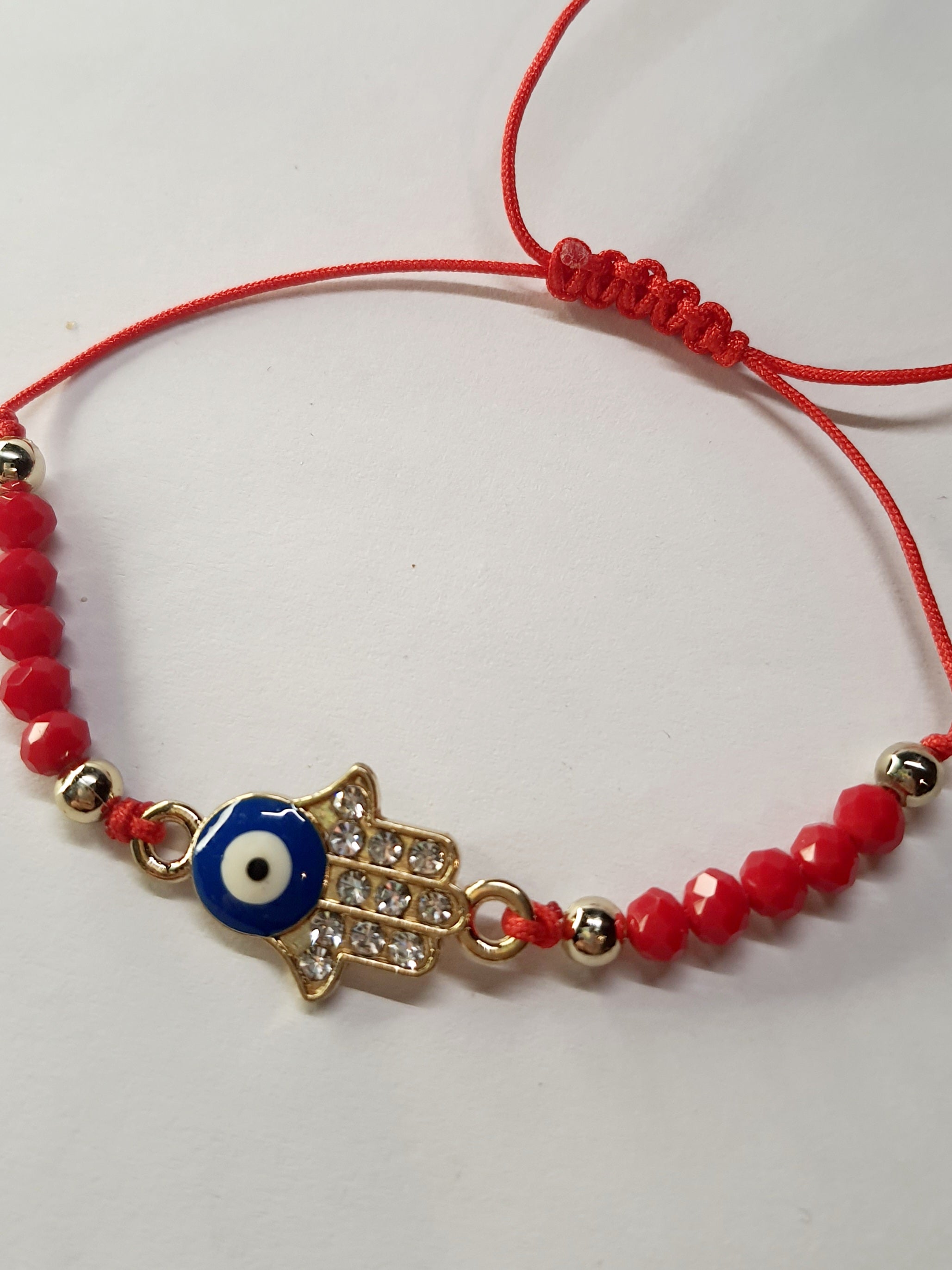 Bransoletka na czerwonym sznurku z zawieszką w kształcie dłoni Fatimy z okiem proroka, zdobioną cyrkoniami. Styl boho i amulet ochronny. Stal chirurgiczna, stal nierdzewna, wodoodporne, hipoalergiczne, jakość premium. Rouge Bizu.