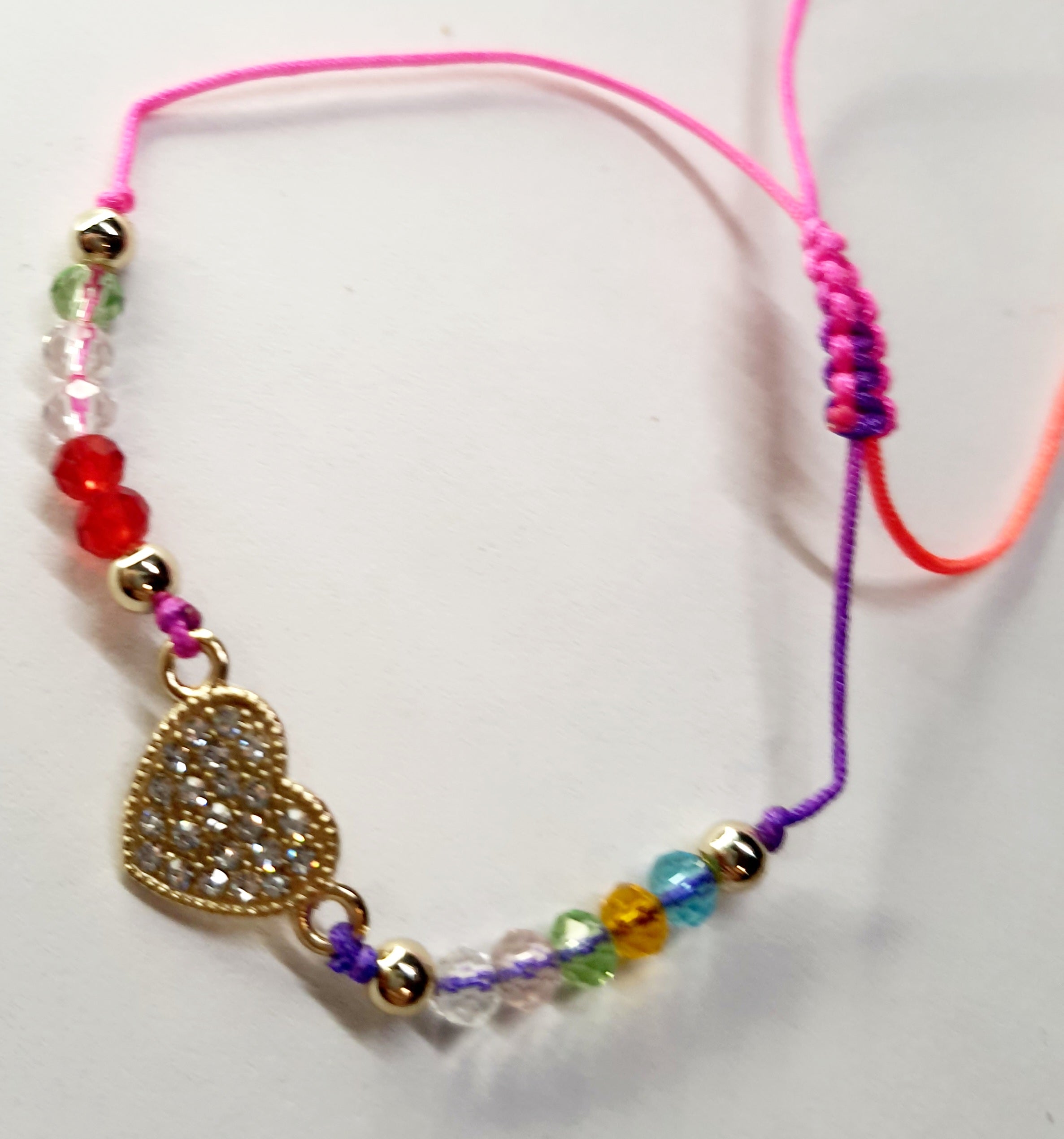 Bransoletka z sercem wysadzanym cyrkoniami na różowo-fioletowym sznurku z kolorowymi koralikami. Delikatna, kolorowa biżuteria w stylu boho, romantyczna i radosna. Wodoodporne, hipoalergiczne, jakość premium. Rouge Bizu.