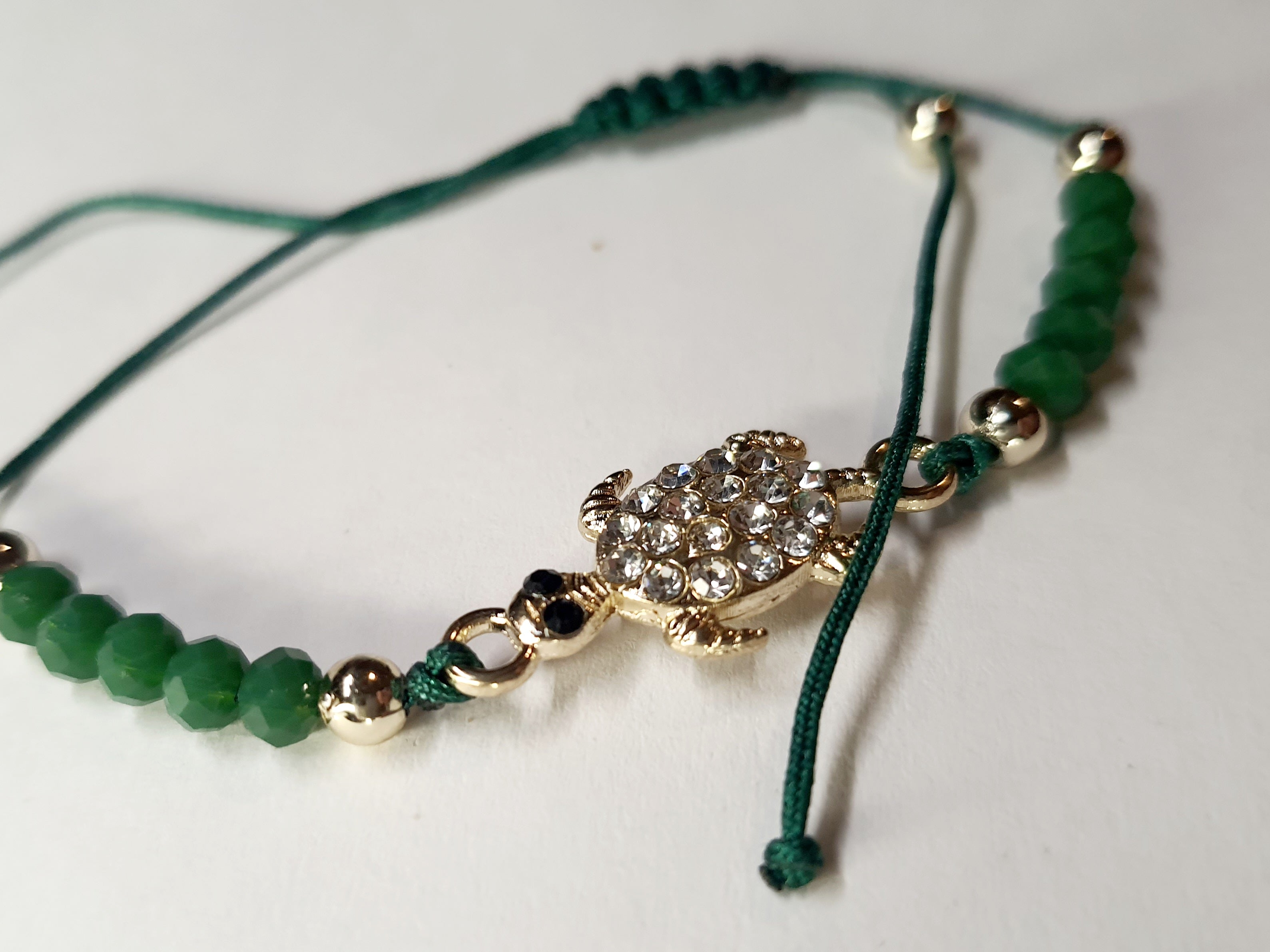 Bransoletka z zawieszką w kształcie żółwia wysadzanego cyrkoniami na zielonym sznurku z zielonymi koralikami. Styl boho, talizman szczęścia i harmonii. Wodoodporne, hipoalergiczne, jakość premium. Rouge Bizu.