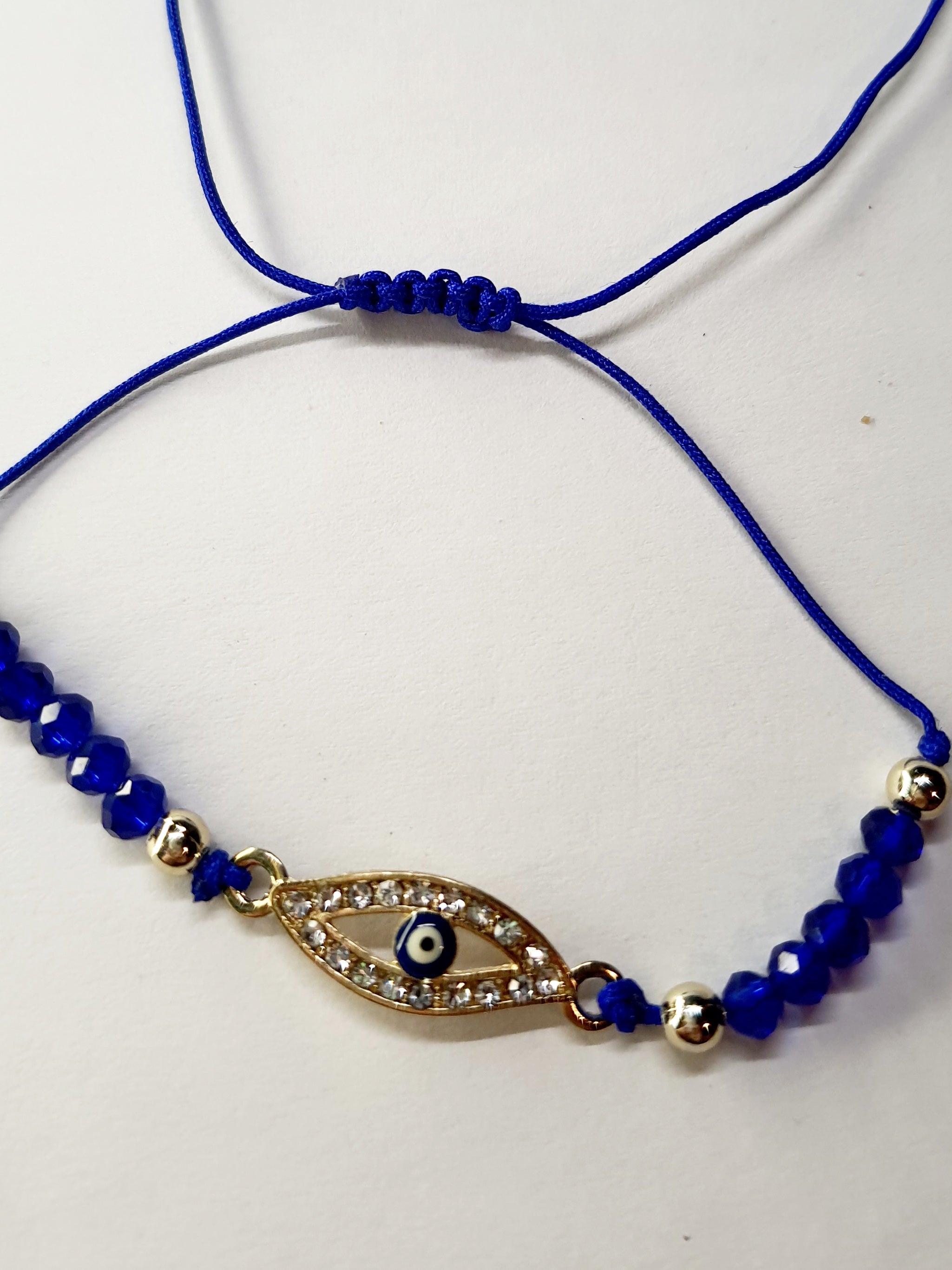 Bransoletka z okiem proroka w złotej oprawie wysadzanej cyrkoniami, na granatowym sznurku z ciemnoniebieskimi koralikami. Elegancka, ochronna biżuteria w stylu boho. Wodoodporne, hipoalergiczne, jakość premium. Rouge Bizu.