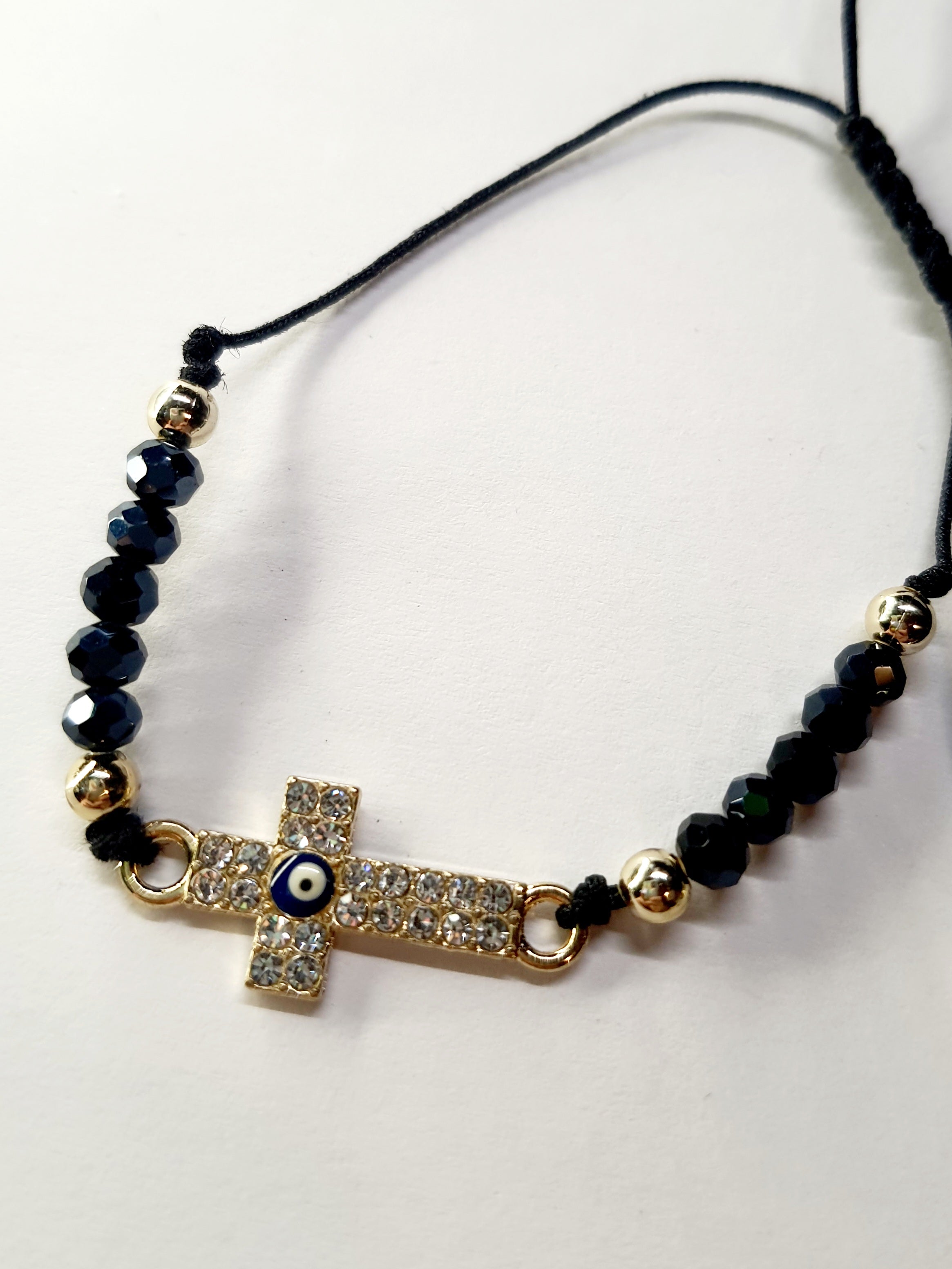 Bransoletka z krzyżem wysadzanym cyrkoniami i okiem proroka w złotej oprawie, na czarnym sznurku z ciemnymi koralikami. Ochronna i elegancka biżuteria w stylu boho. Wodoodporne, hipoalergiczne, jakość premium. Rouge Bizu.