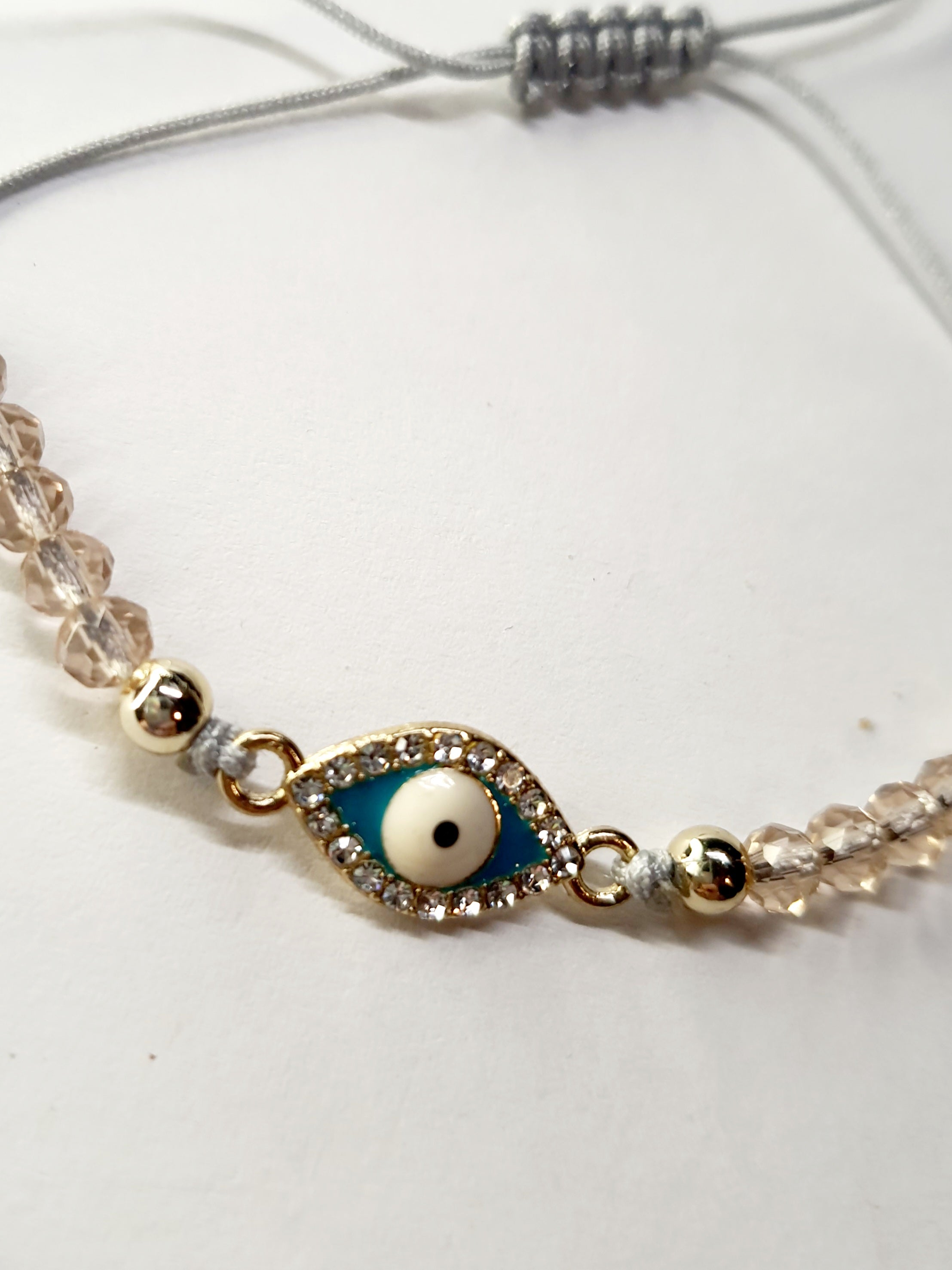 Bransoletka z turkusowym okiem proroka w złotej oprawie wysadzanej cyrkoniami, na różowym sznurku z przezroczystymi koralikami. Delikatna, ochronna biżuteria w stylu boho. Wodoodporne, hipoalergiczne, jakość premium. Rouge Bizu.