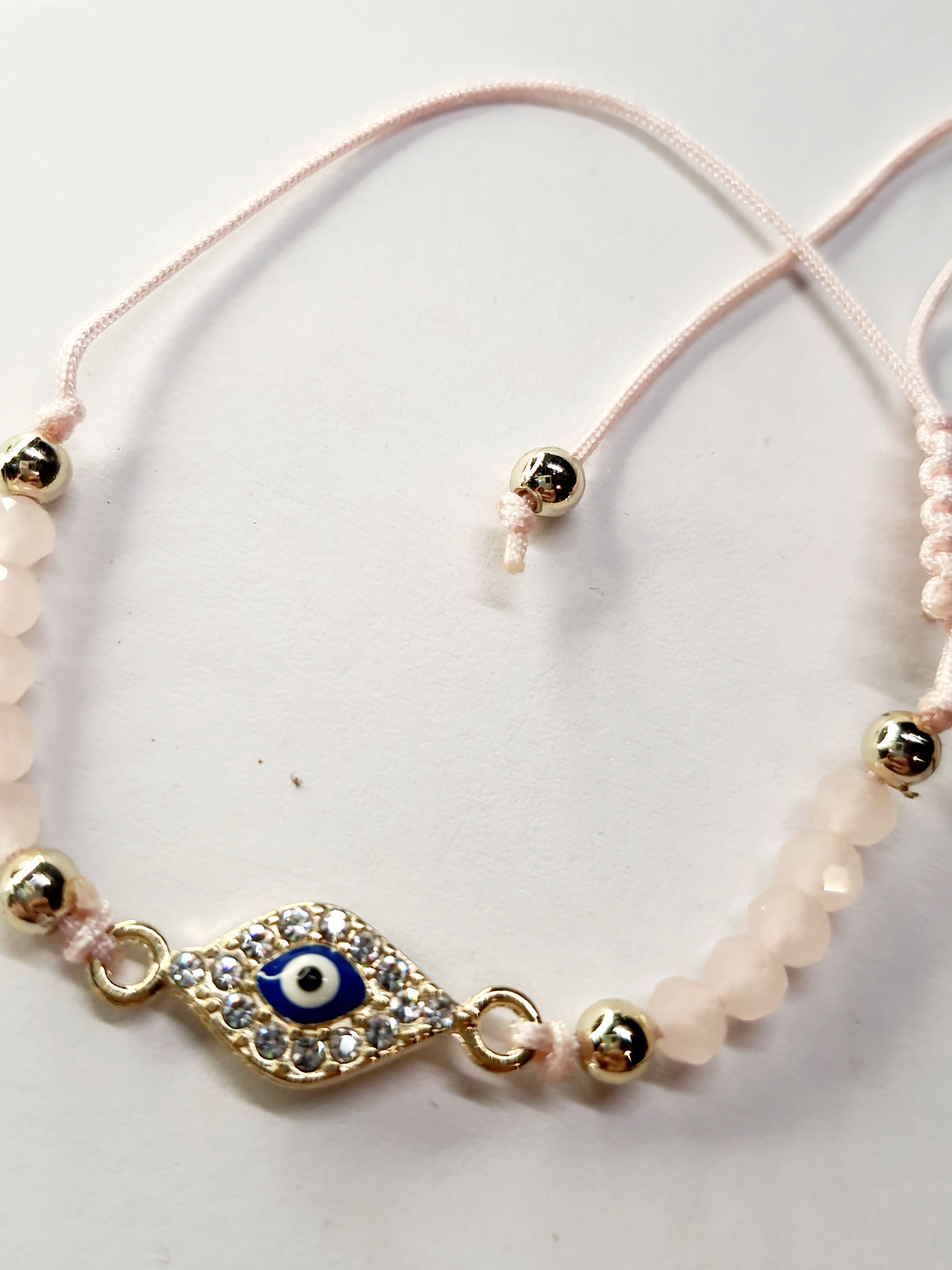 Bransoletka z okiem proroka w złotej oprawie wysadzanej cyrkoniami, na pudroworóżowym sznurku z matowymi różowymi koralikami. Delikatna, kobieca biżuteria ochronna w stylu boho. Wodoodporne, hipoalergiczne, jakość premium. Rouge Bizu.