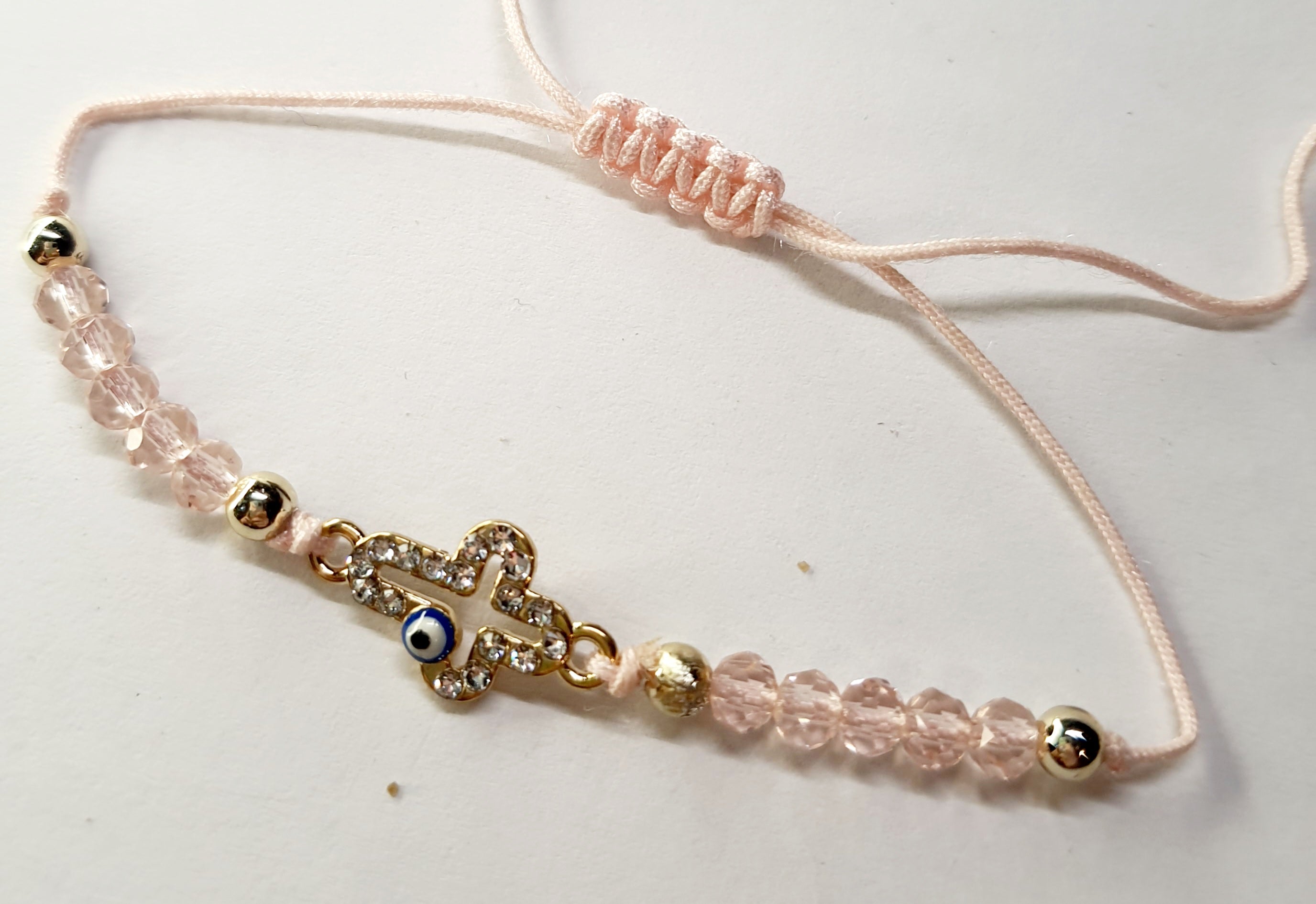 Bransoletka z krzyżem wysadzanym cyrkoniami i okiem proroka, na pudroworóżowym sznurku z różowymi koralikami. Delikatna, elegancka biżuteria ochronna w stylu boho. Wodoodporne, hipoalergiczne, jakość premium. Rouge Bizu.