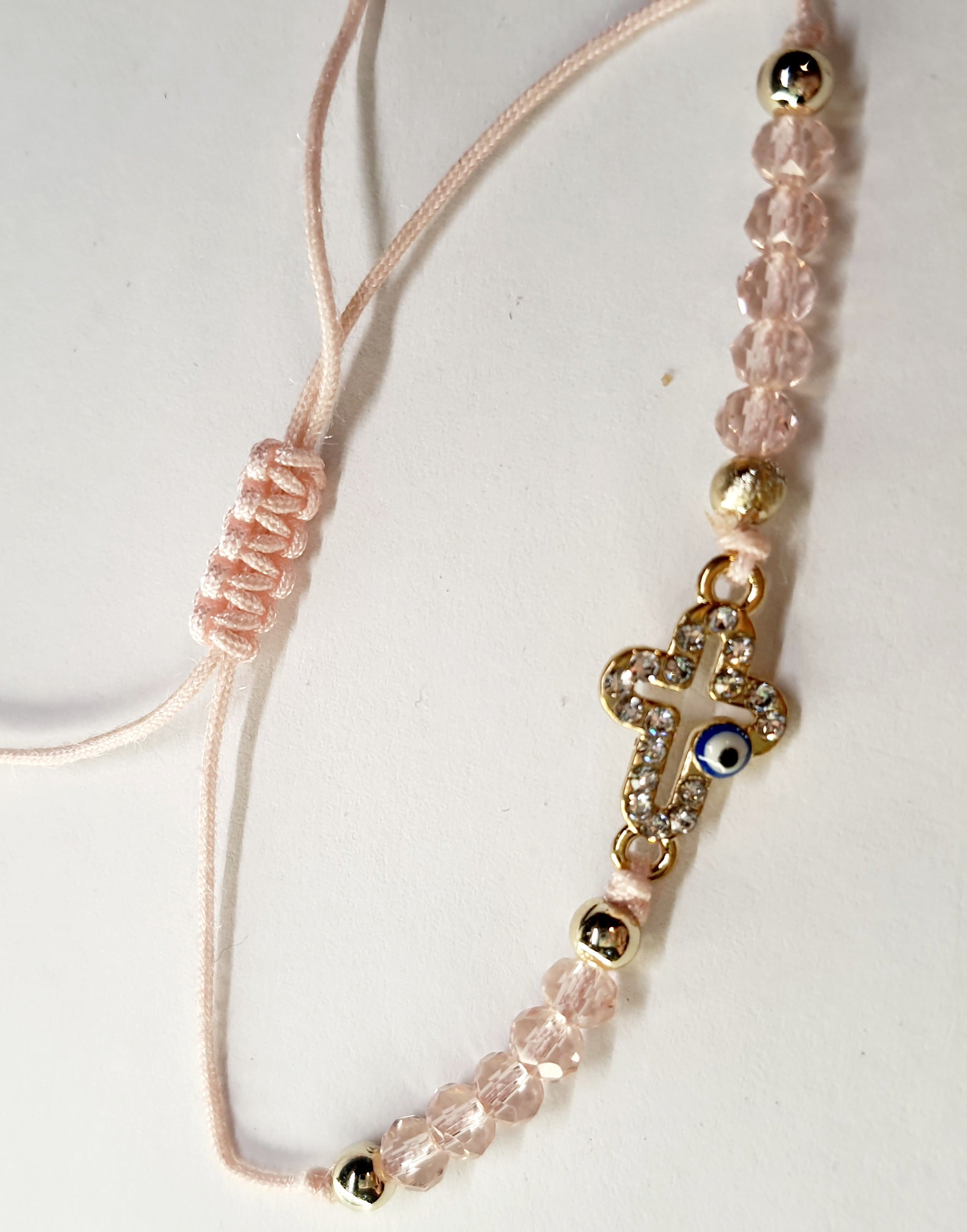 Bransoletka z krzyżem wysadzanym cyrkoniami i okiem proroka, na pudroworóżowym sznurku z różowymi koralikami. Delikatna, elegancka biżuteria ochronna w stylu boho. Wodoodporne, hipoalergiczne, jakość premium. Rouge Bizu.