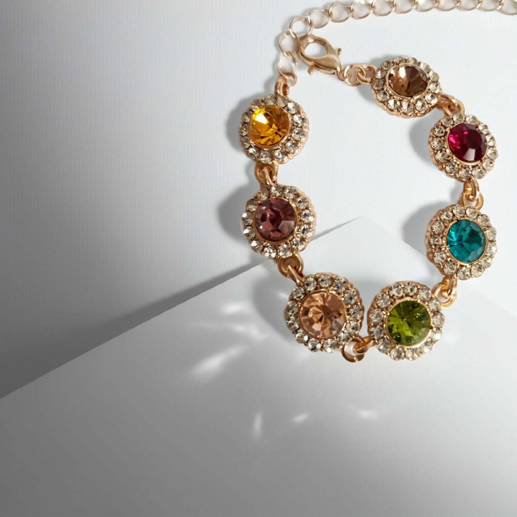Bransoletka ze stali nierdzewnej w kolorze złota, z okrągłymi kolorowymi kryształami w odcieniach czerwieni, turkusu, zieleni, złota i bursztynu, otoczonymi małymi cyrkoniami. Długość regulowana 25 cm. Rouge Bizu.