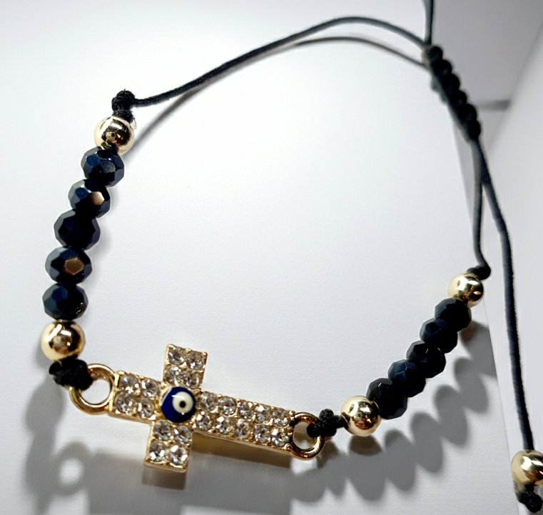 Bransoletka z krzyżem wysadzanym cyrkoniami i okiem proroka w złotej oprawie, na czarnym sznurku z ciemnymi koralikami. Ochronna i elegancka biżuteria w stylu boho. Wodoodporne, hipoalergiczne, jakość premium. Rouge Bizu.