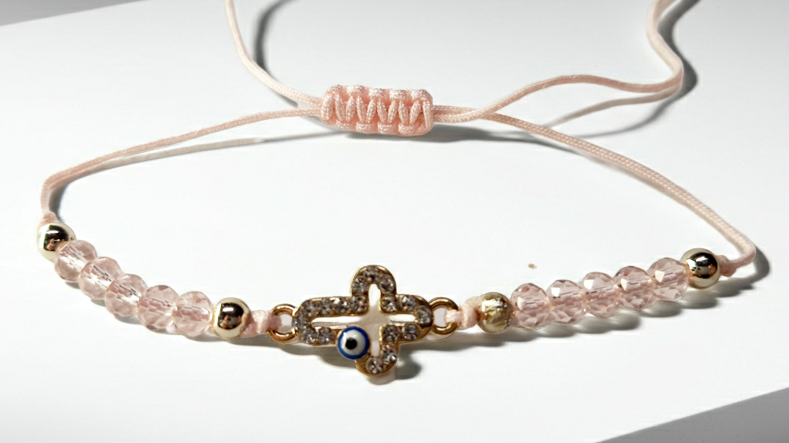 Bransoletka z krzyżem wysadzanym cyrkoniami i okiem proroka, na pudroworóżowym sznurku z różowymi koralikami. Delikatna, elegancka biżuteria ochronna w stylu boho. Wodoodporne, hipoalergiczne, jakość premium. Rouge Bizu.