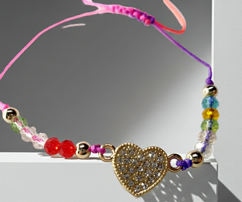 Bransoletka z sercem wysadzanym cyrkoniami na różowo-fioletowym sznurku z kolorowymi koralikami. Delikatna, kolorowa biżuteria w stylu boho, romantyczna i radosna. Wodoodporne, hipoalergiczne, jakość premium. Rouge Bizu.