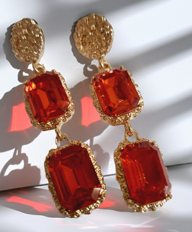 Długie kolczyki ze stali nierdzewnej w stylu glamour, ozdobione dużymi czerwonymi kamieniami w złotej oprawie. Elegancja, luksus i ognisty blask. Długość 7 cm. Rouge Bizu.