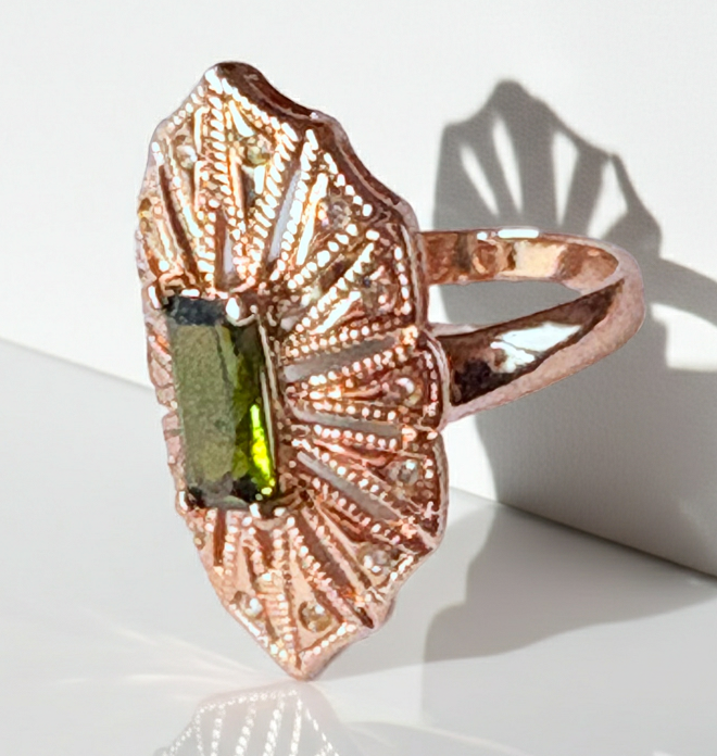 Pierścionek z podłużnym szmaragdowym kamieniem w stylu glamour vintage, oprawiony w wachlarz różowozłotych detali z drobnymi cyrkoniami. Rozmiar 20 mm. Elegancki, kobiecy, wykonany ze stali chirurgicznej. Rouge Bizu.