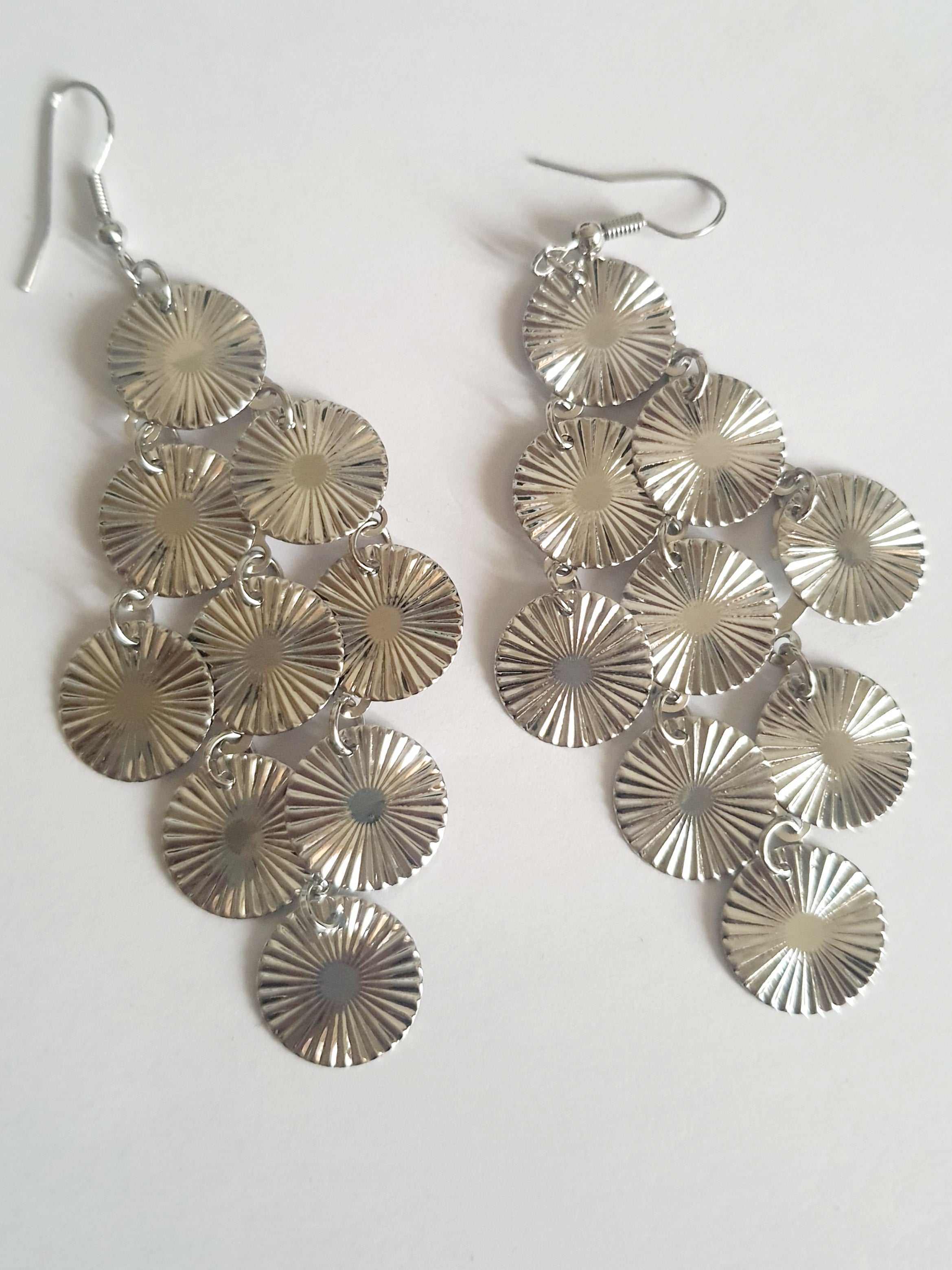 Srebrne kolczyki wiszące z promienistych dysków na biglu, wykonane ze stali nierdzewnej. Lekka, ruchoma forma z błyszczącym wykończeniem. Styl glamour i elegancja. Rouge Bizu.

