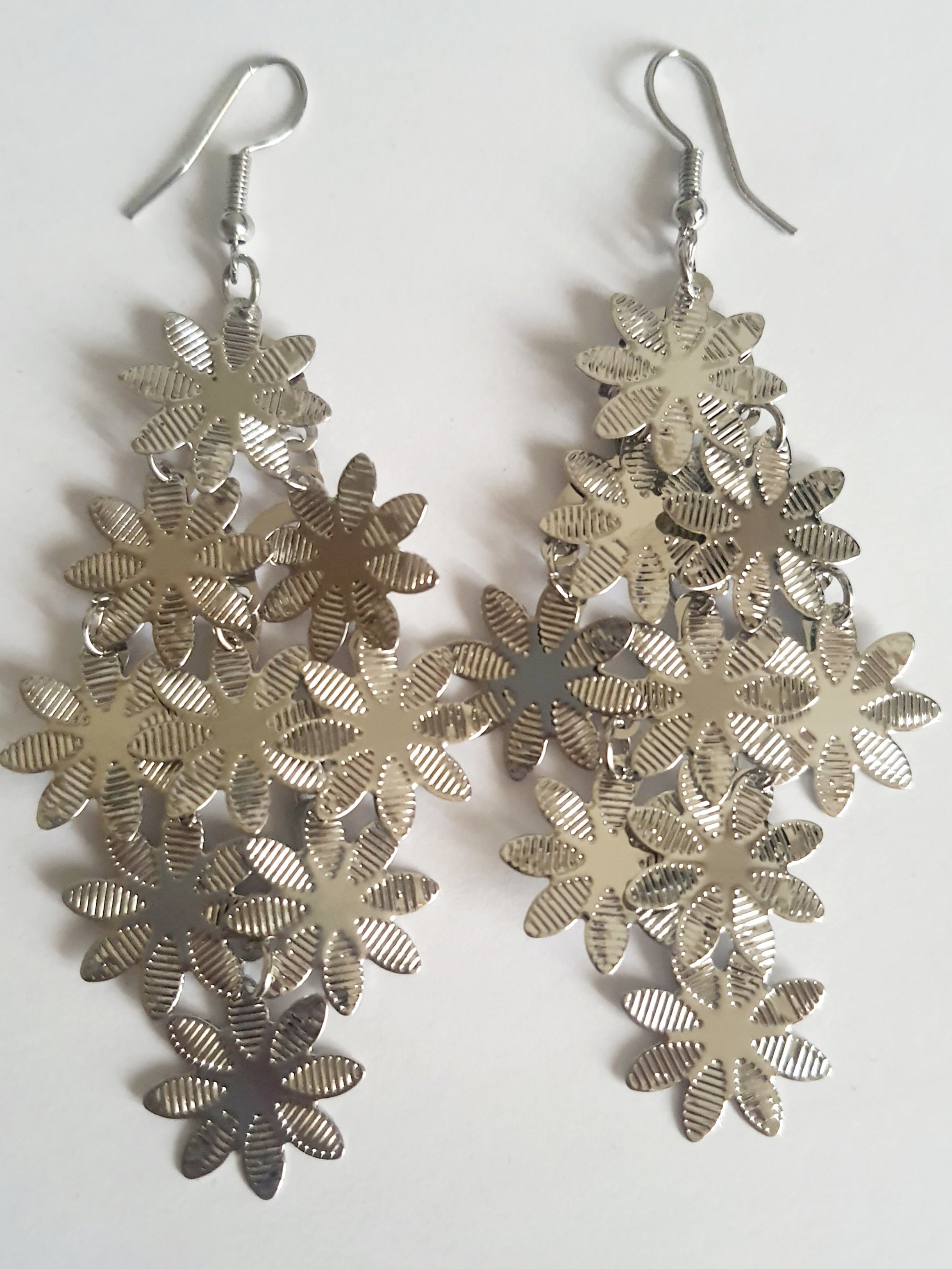 Wiszące kolczyki ze stali nierdzewnej w kolorze srebrnym. Ażurowe wzory kwiatków, zapięcie na bigiel. Lekkie, błyszczące, romantyczne akcenty inspirowane naturą. Rouge Bizu.

