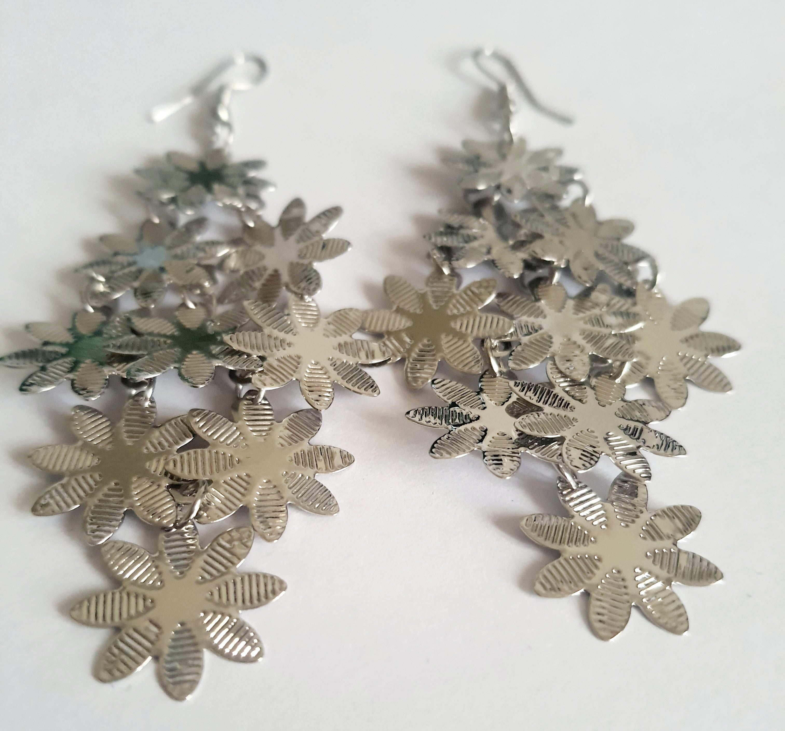 Wiszące kolczyki ze stali nierdzewnej w kolorze srebrnym. Ażurowe wzory kwiatków, zapięcie na bigiel. Lekkie, błyszczące, romantyczne akcenty inspirowane naturą. Rouge Bizu.

