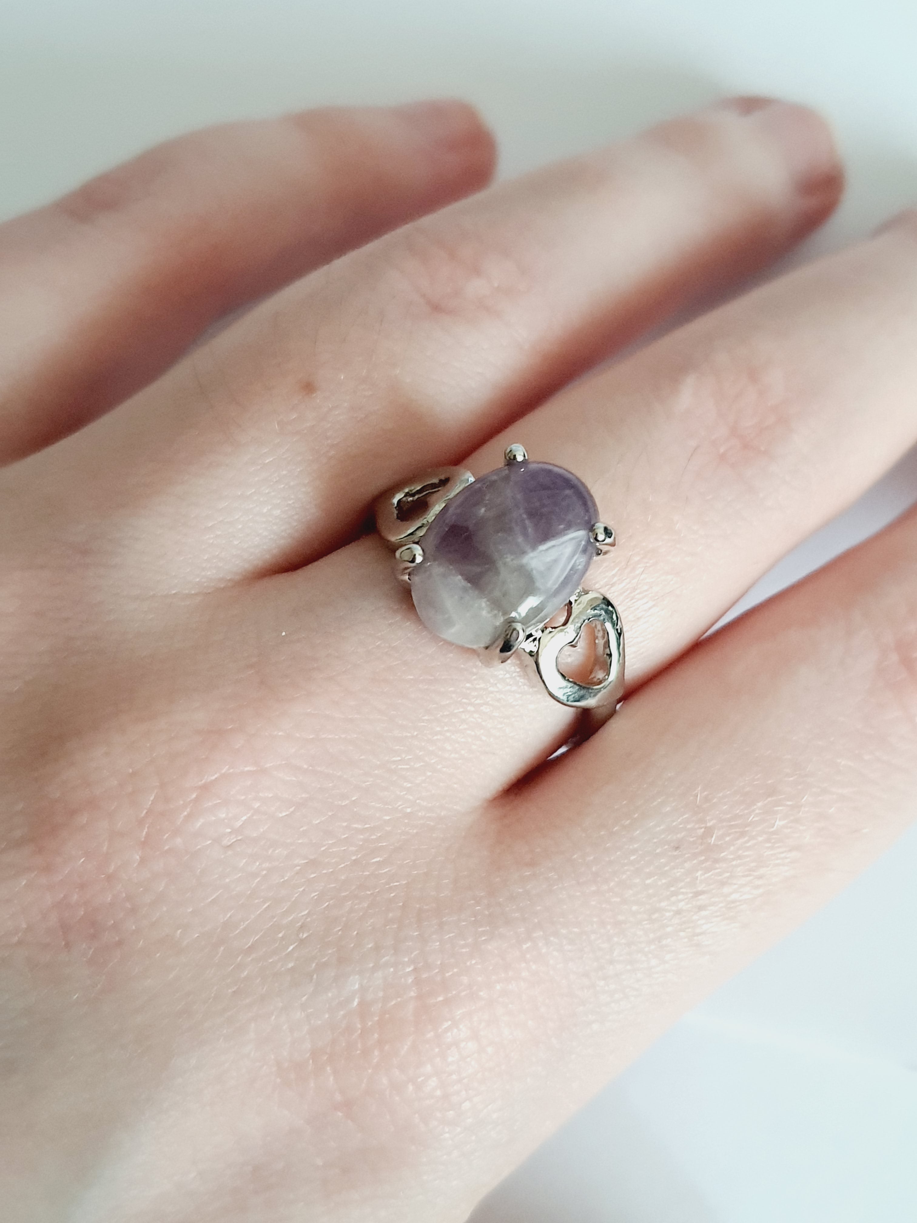 Srebrny pierścionek ze stali nierdzewnej z owalnym kamieniem w odcieniu lila i ozdobnym wycięciem po bokach. Styl romantyczny, artystyczny. Rozmiar 20 mm. Rouge Bizu.

