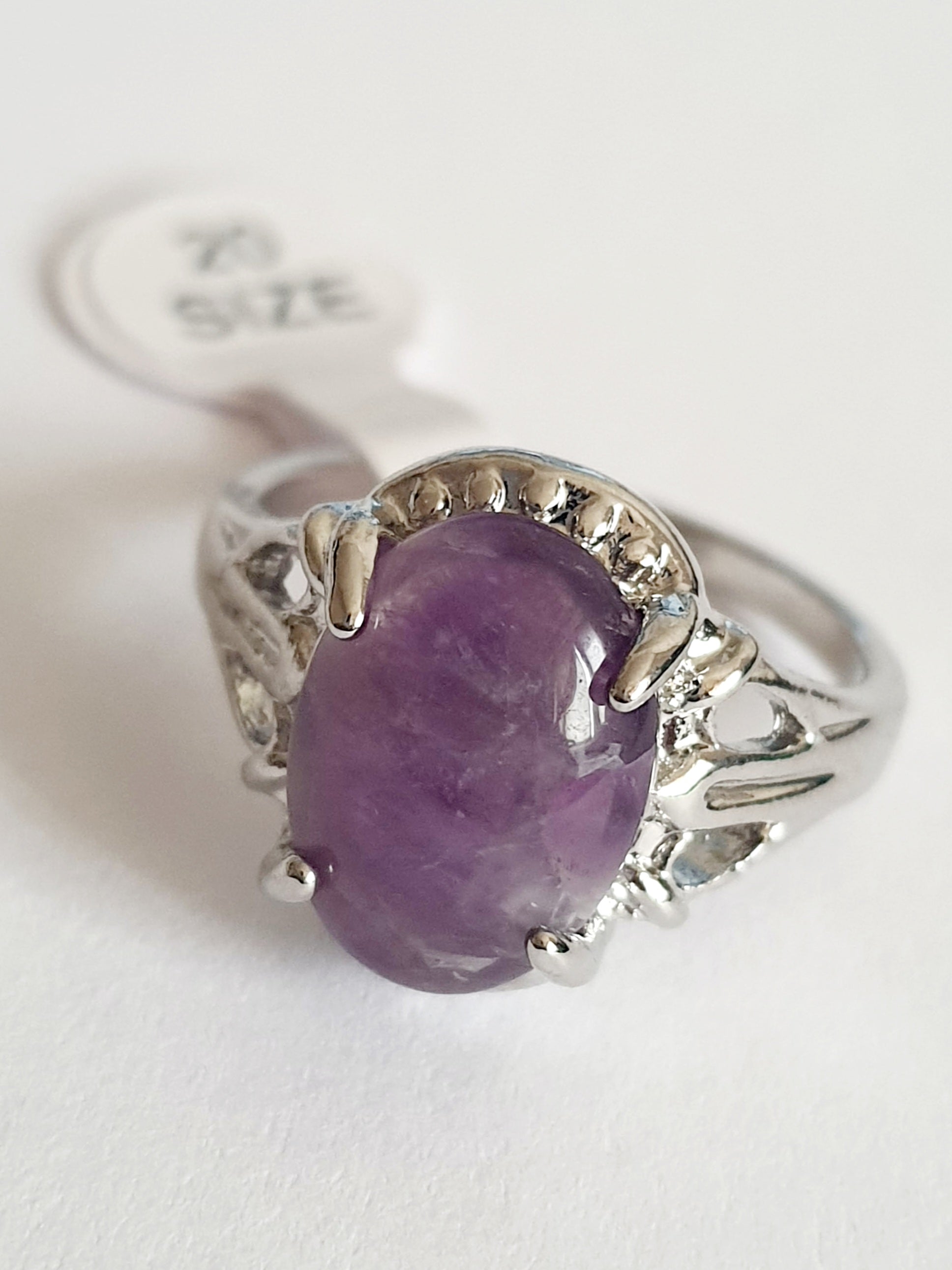 Pierścionek ze stali nierdzewnej z dużym owalnym kamieniem w odcieniu lila (imitacja ametystu), srebrna oprawa z dekoracyjnymi wycięciami, styl vintage glamour, rozmiar 20 mm. Rouge Bizu.

