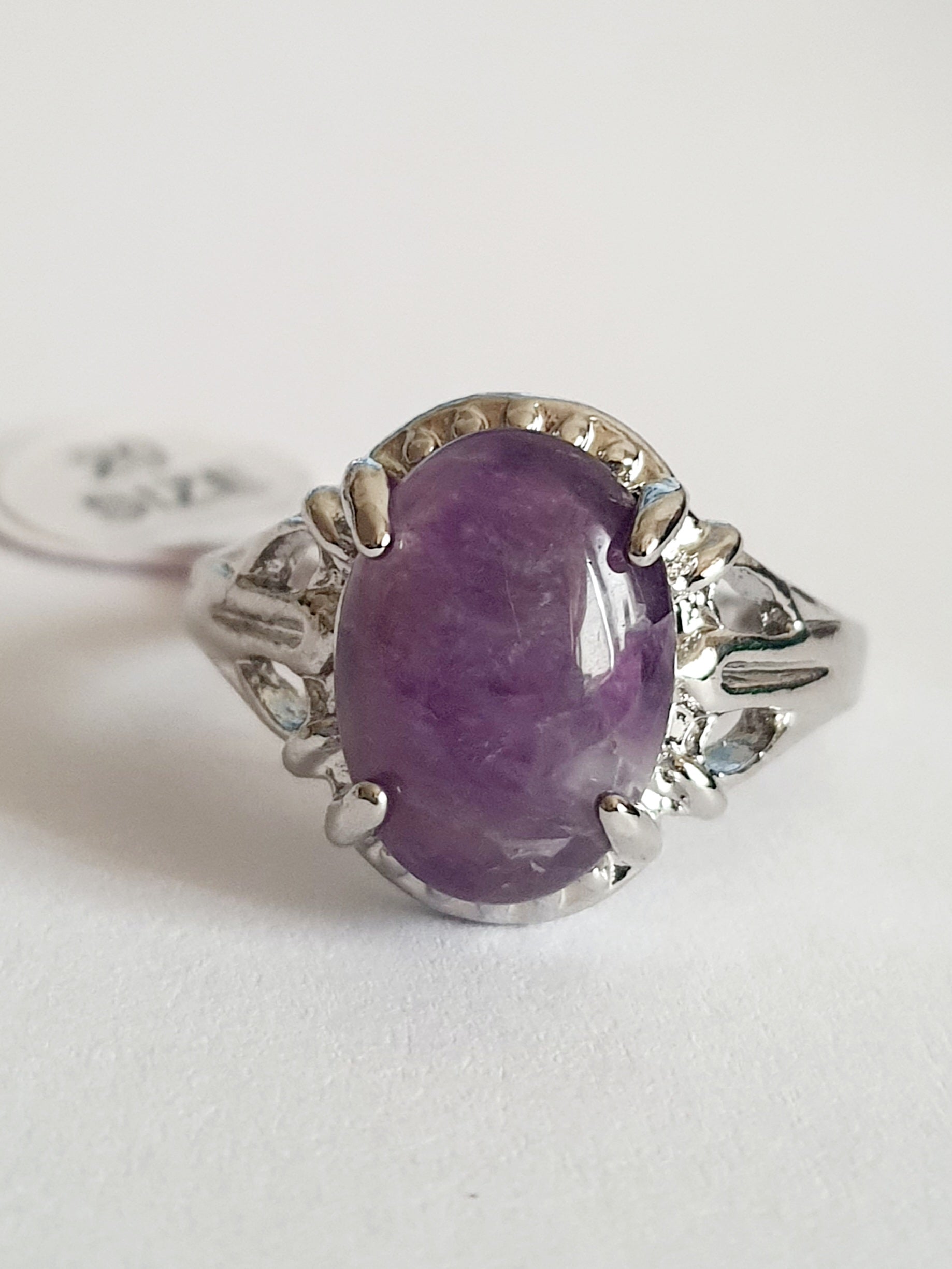 Pierścionek ze stali nierdzewnej z dużym owalnym kamieniem w odcieniu lila (imitacja ametystu), srebrna oprawa z dekoracyjnymi wycięciami, styl vintage glamour, rozmiar 20 mm. Rouge Bizu.

