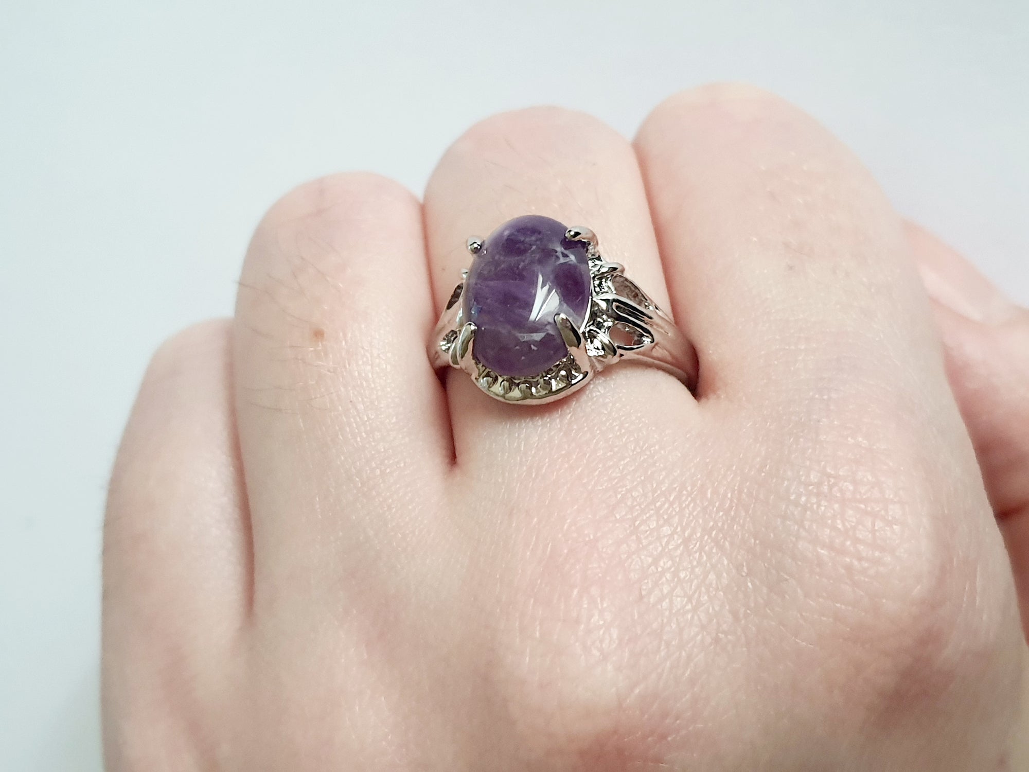 Pierścionek ze stali nierdzewnej z dużym owalnym kamieniem w odcieniu lila (imitacja ametystu), srebrna oprawa z dekoracyjnymi wycięciami, styl vintage glamour, rozmiar 20 mm. Rouge Bizu.

