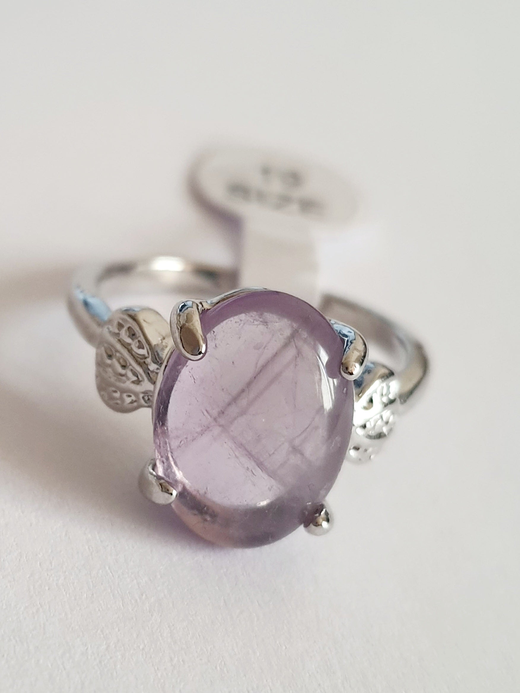 Pierścionek ze stali chirurgicznej w srebrnym kolorze z jasnofioletowym, owalnym kamieniem w stylu ametystu. Boczne elementy w kształcie liści. Styl romantyczny i subtelny. Rozmiar 19 mm. Rouge Bizu.

