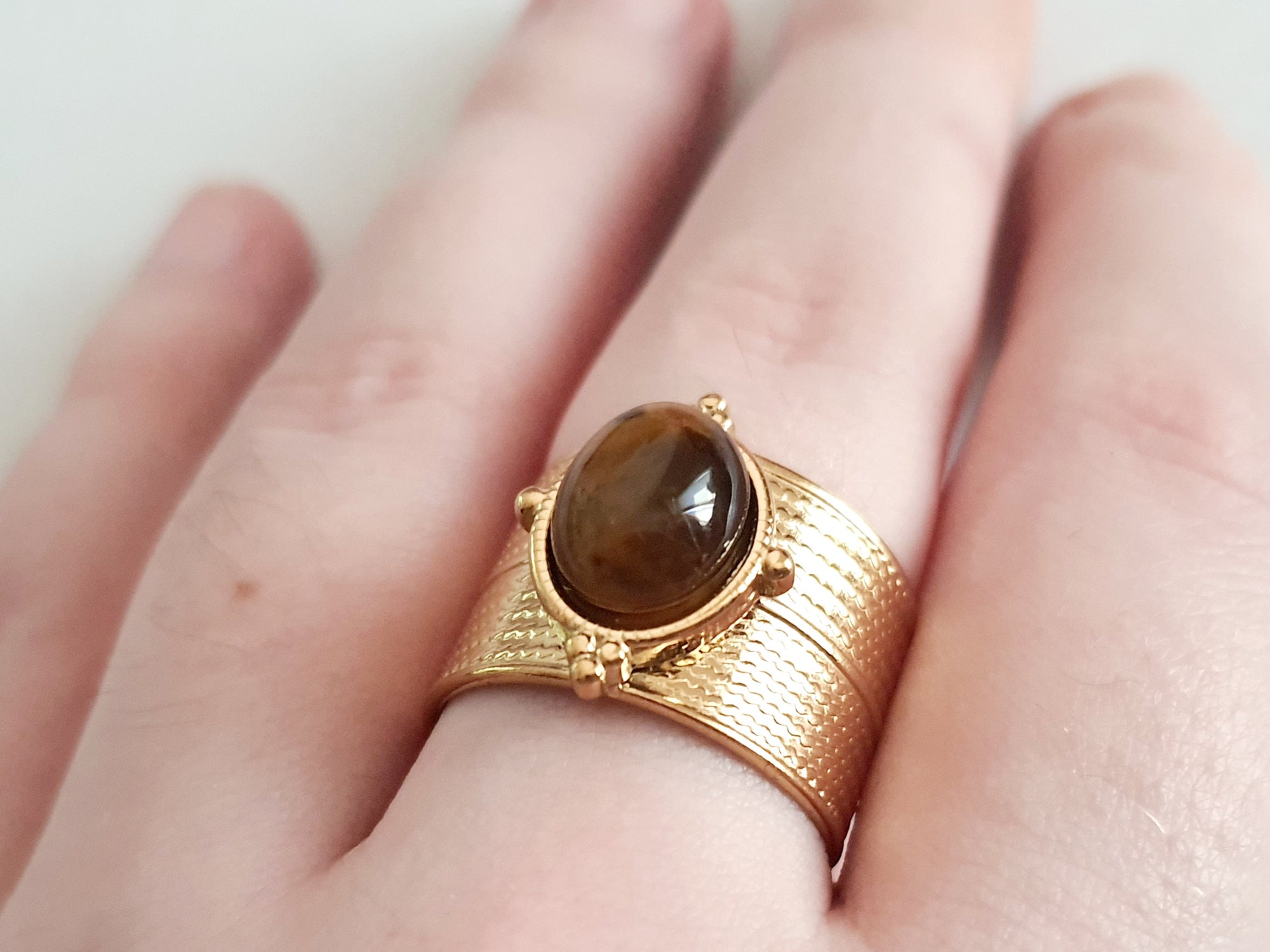Pierścionek w kolorze złota z szeroką obrączką i syntetycznym kamieniem przypominającym tygrysie oko, stal chirurgiczna, rozmiar 19 mm.

