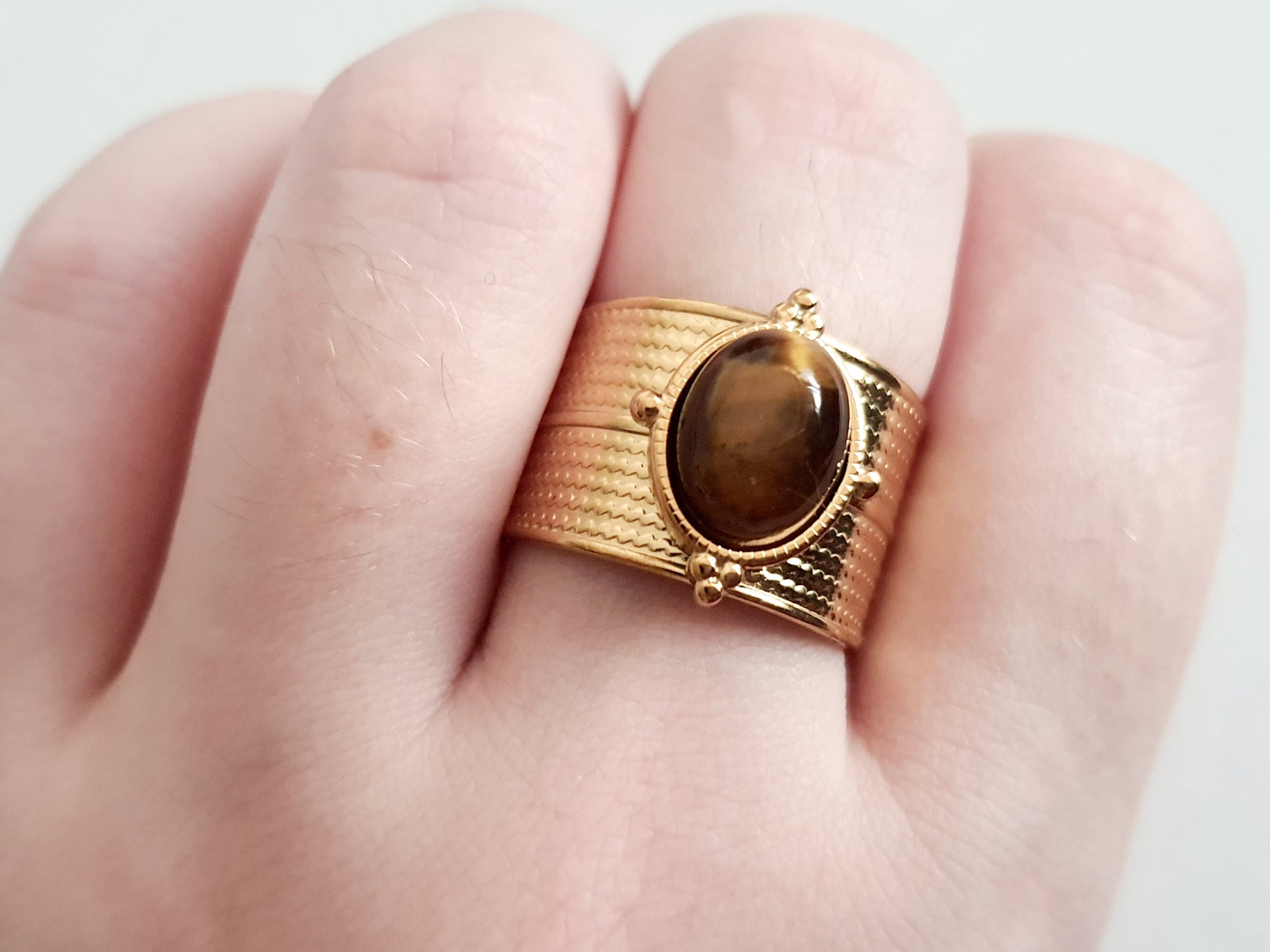 Pierścionek w kolorze złota z szeroką obrączką i syntetycznym kamieniem przypominającym tygrysie oko, stal chirurgiczna, rozmiar 19 mm.

