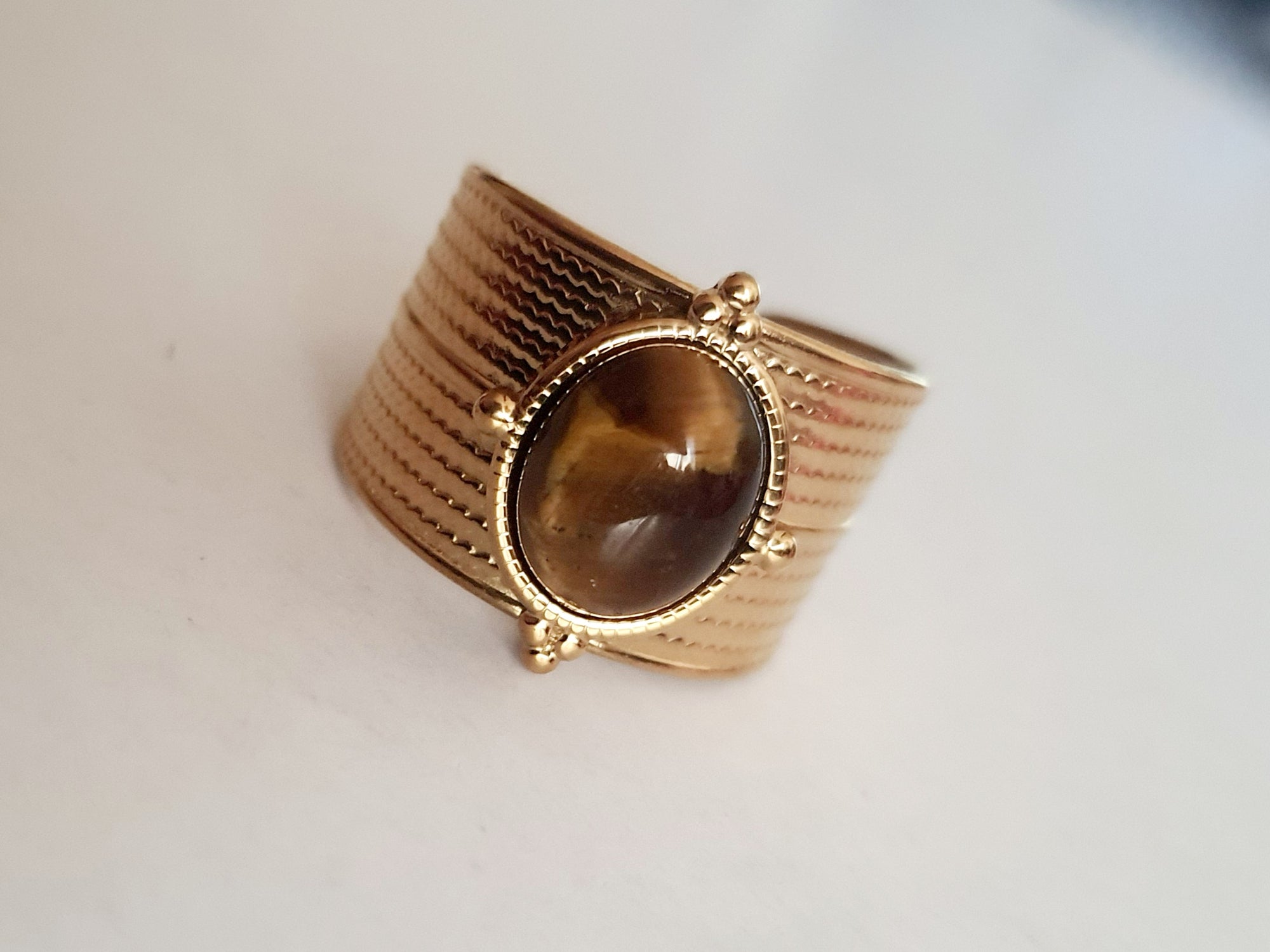 Pierścionek w kolorze złota z szeroką obrączką i syntetycznym kamieniem przypominającym tygrysie oko, stal chirurgiczna, rozmiar 19 mm.

