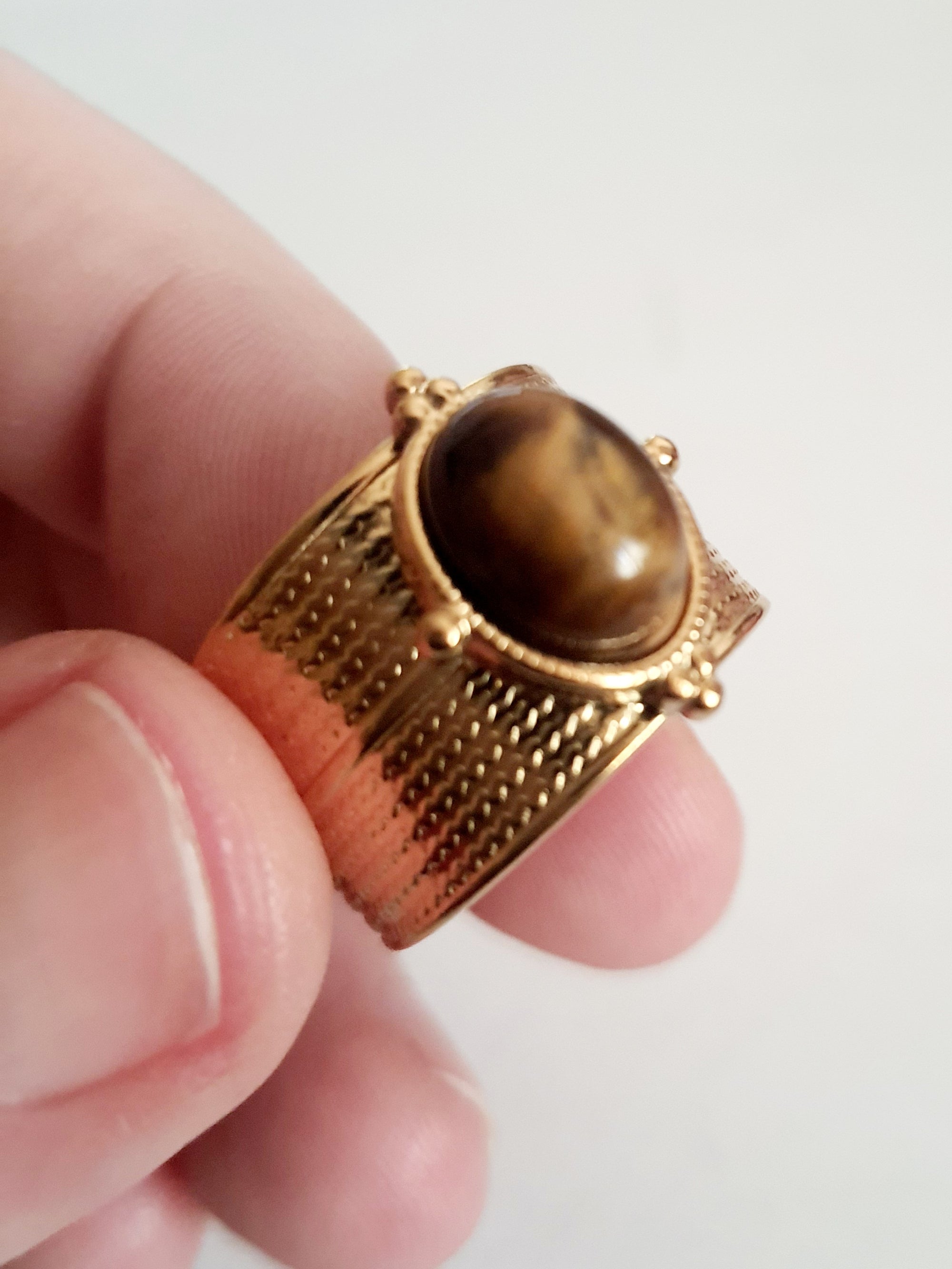 Pierścionek w kolorze złota z szeroką obrączką i syntetycznym kamieniem przypominającym tygrysie oko, stal chirurgiczna, rozmiar 19 mm.

