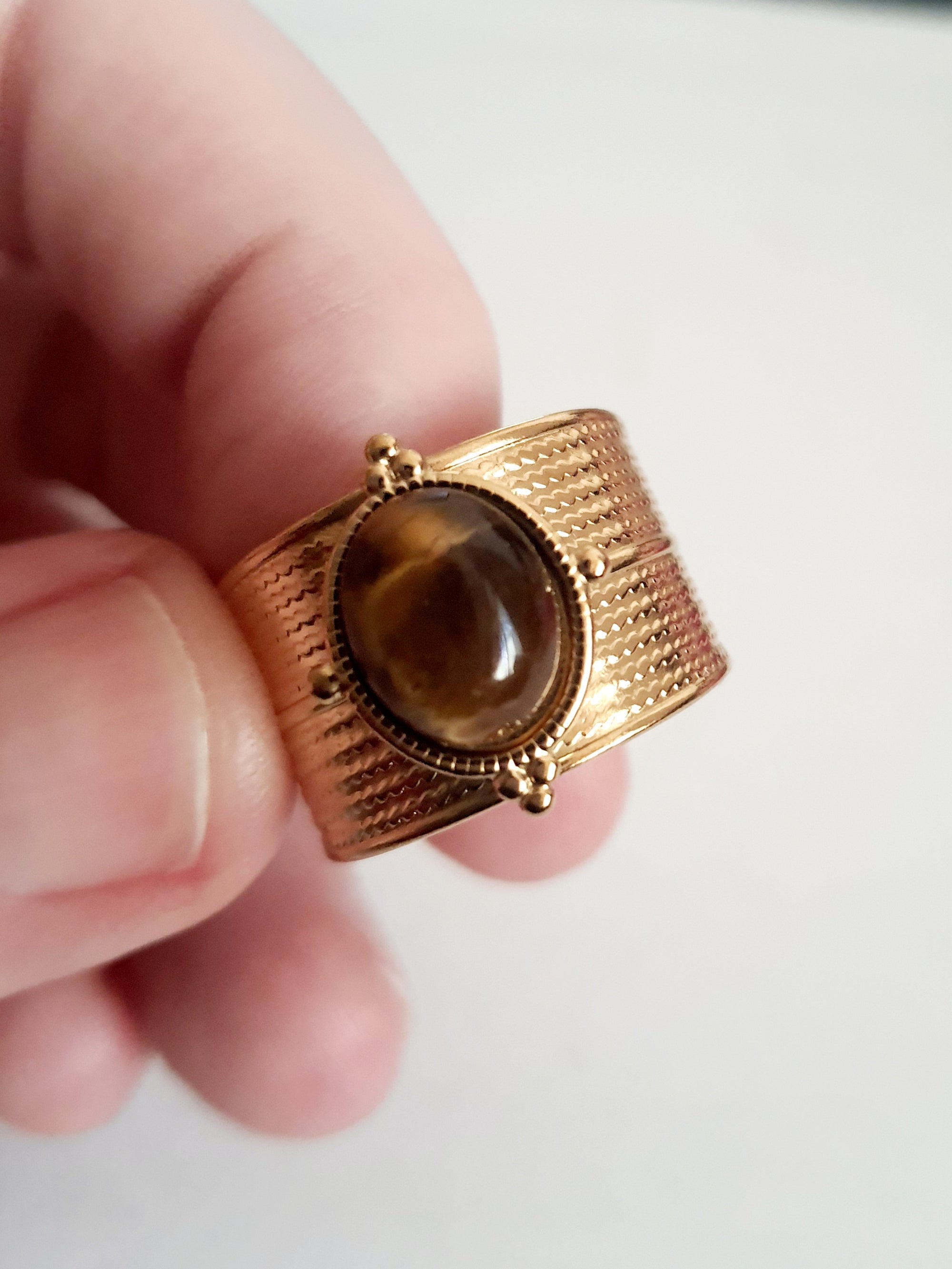 Pierścionek w kolorze złota z szeroką obrączką i syntetycznym kamieniem przypominającym tygrysie oko, stal chirurgiczna, rozmiar 19 mm.

