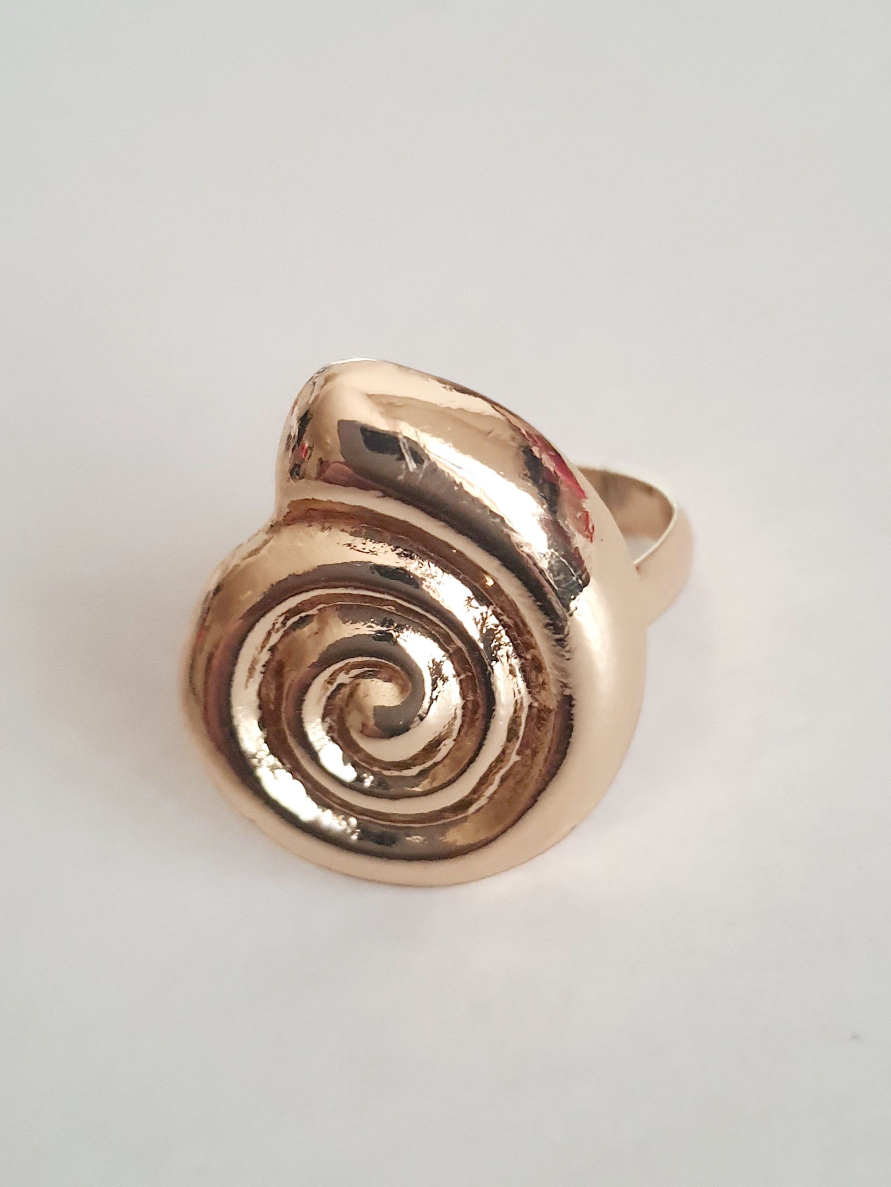 Pierścionek spiralny ze stali nierdzewnej w kolorze żółtego złota, z błyszczącym wykończeniem i efektownym, hipnotyzującym kształtem spirali. Styl minimalistyczny z nutą artystycznej ekstrawagancji. Regulowany rozmiar. Rouge Bizu.

