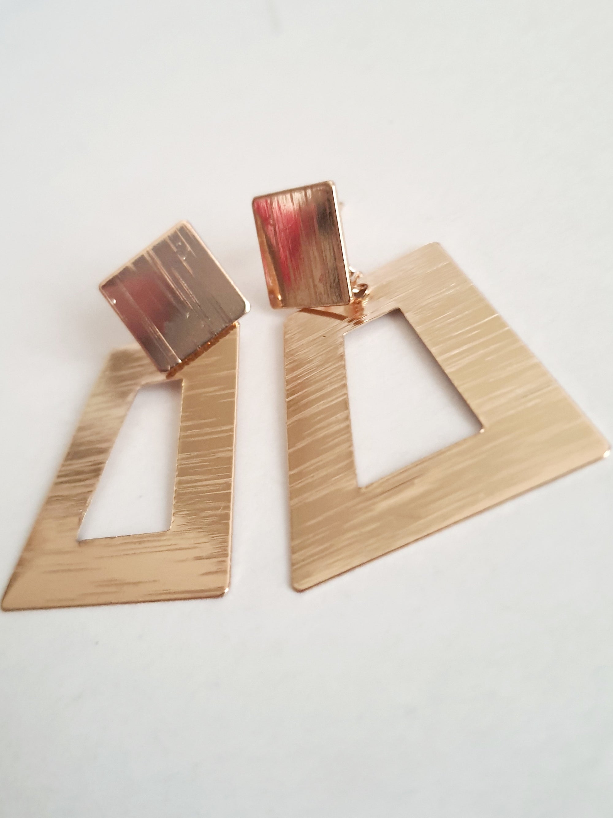 Geometryczne kolczyki z różowego złota o długości 5 cm, wykonane ze stali nierdzewnej. Trapez z wycięciem i kwadratowa baza w formie wkrętki. Nowoczesny, minimalistyczny design w stylu art deco. Rouge Bizu.

