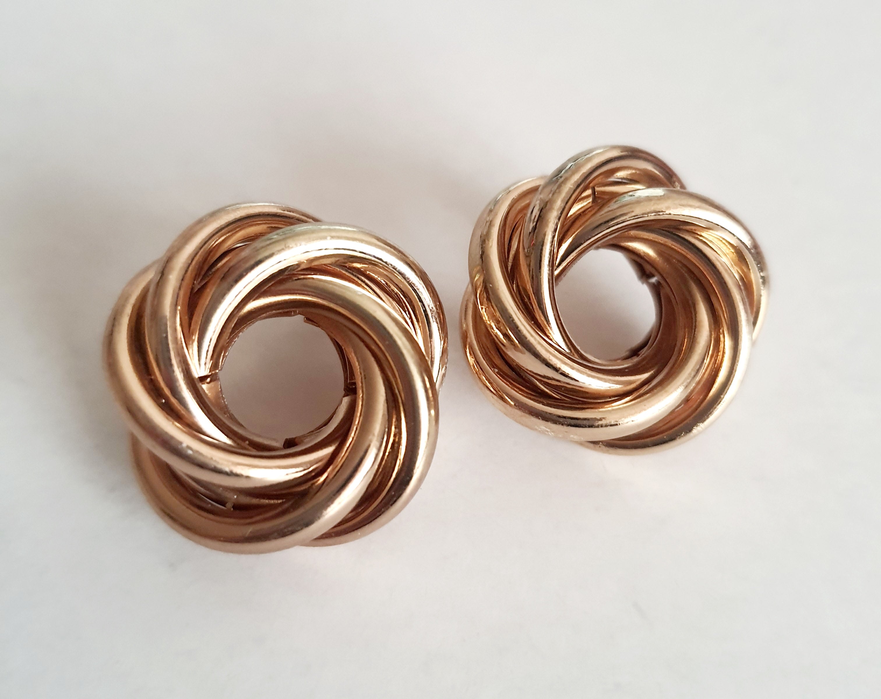 Złote kolczyki wkrętki o średnicy 2 cm, z przeplatającym się węzłem z polerowanych obręczy. Klasyczny splot, elegancja i minimalizm. Stal nierdzewna, Rouge Bizu.

