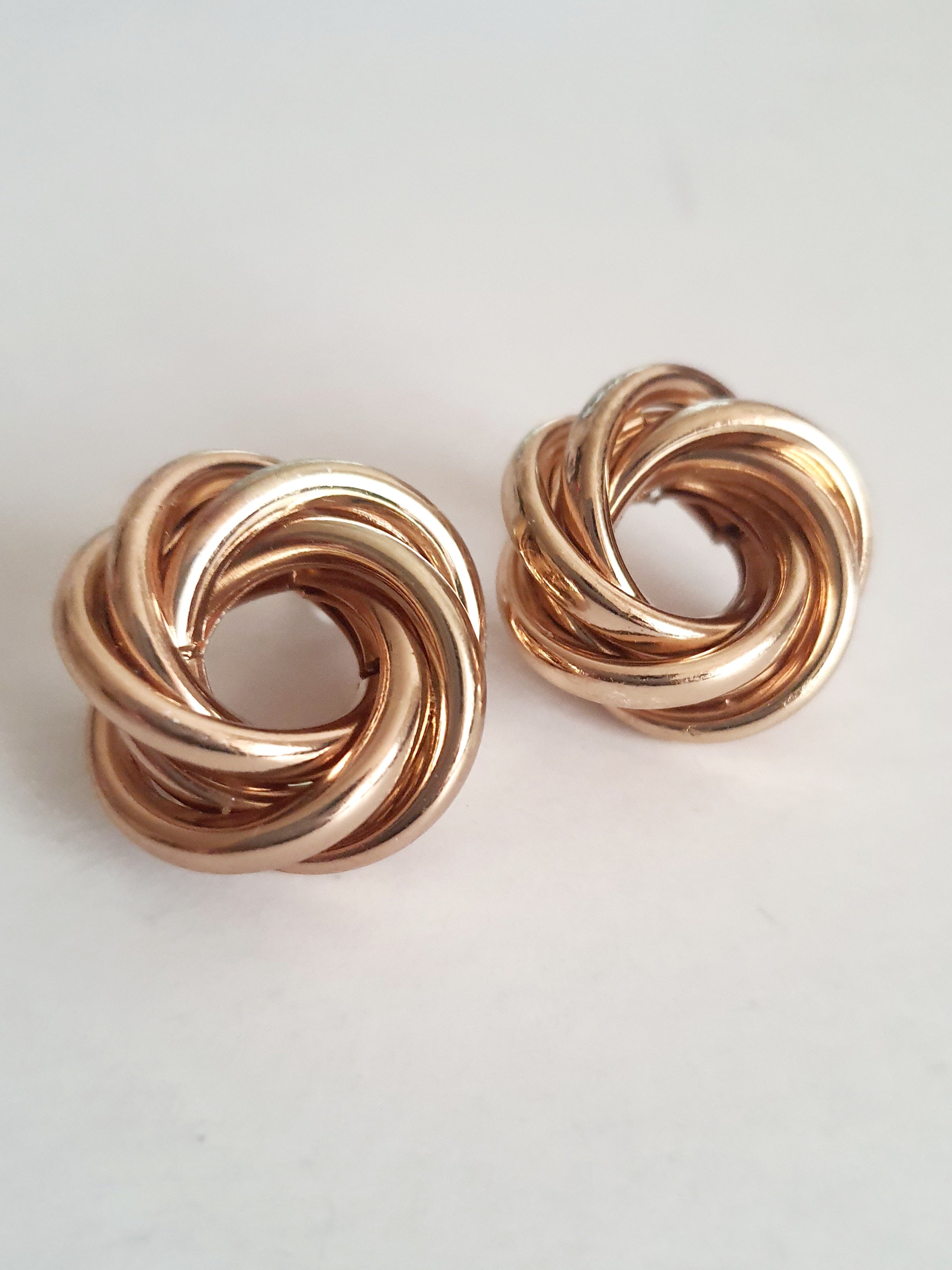 Złote kolczyki wkrętki o średnicy 2 cm, z przeplatającym się węzłem z polerowanych obręczy. Klasyczny splot, elegancja i minimalizm. Stal nierdzewna, Rouge Bizu.

