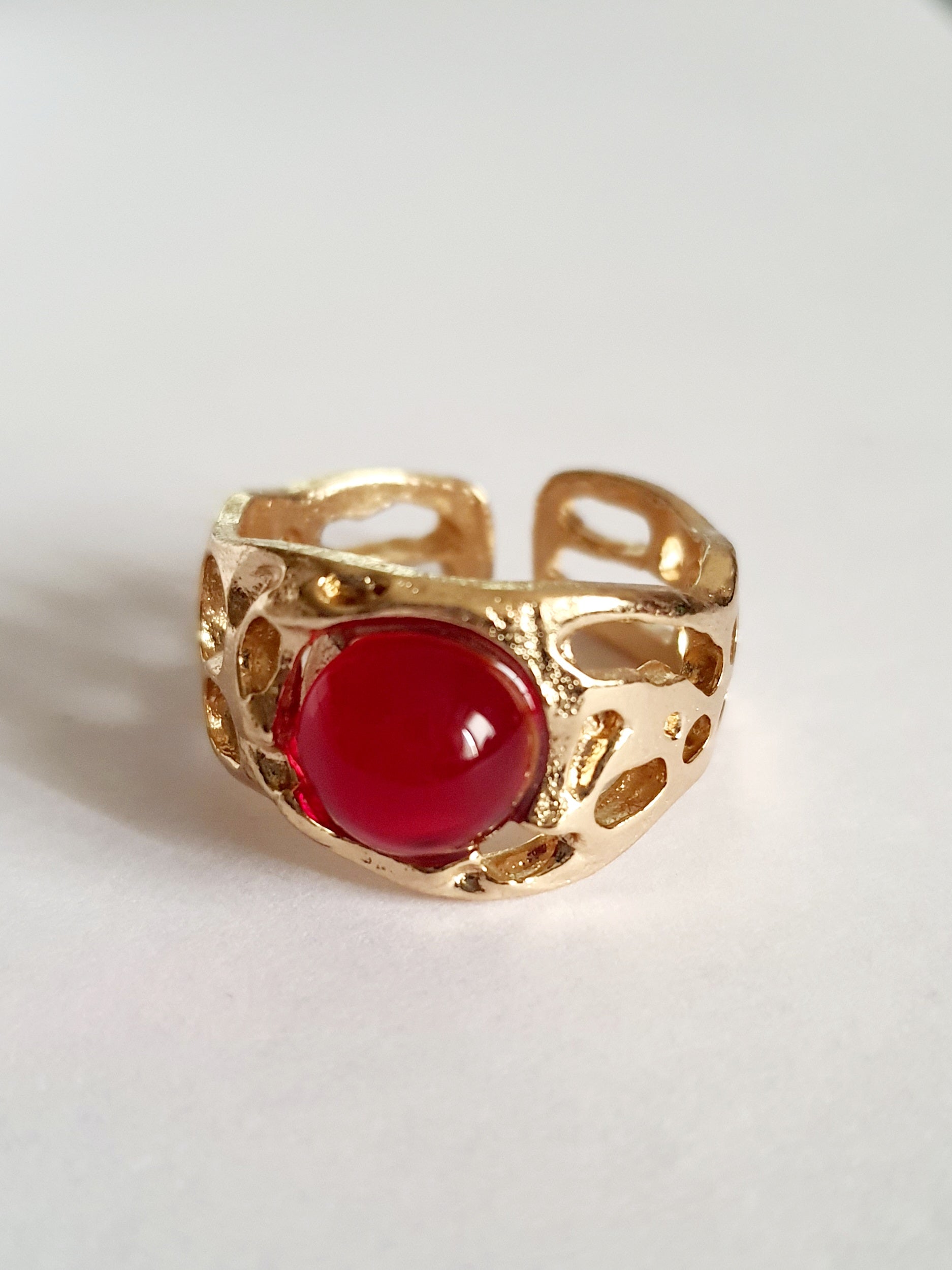 Złoty pierścionek artystyczny z czerwonym kaboszonem, stal nierdzewna, ażurowa forma, rozmiar 16 mm, elegancki i wyrazisty. Rouge Bizu.

